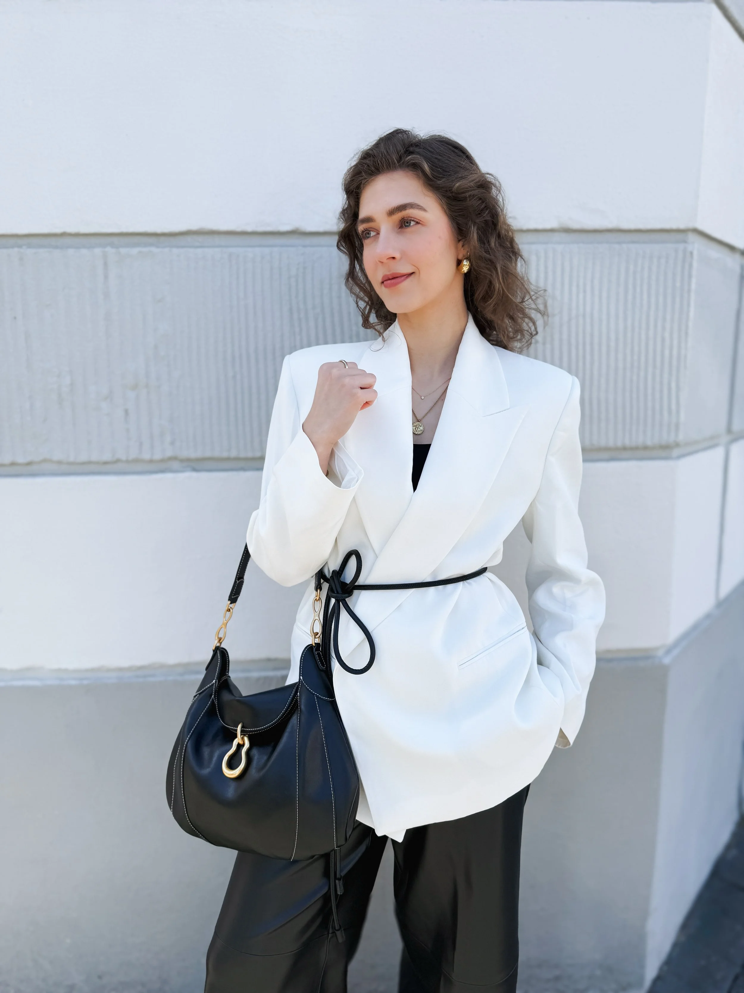 Luise Albrecht von The Neutral Blazer mit einem weißen Blazer zu einer schwarzen Hose mit einer schwarzen Ledertasche von JW PEI und einem schwarzen Gürtel.