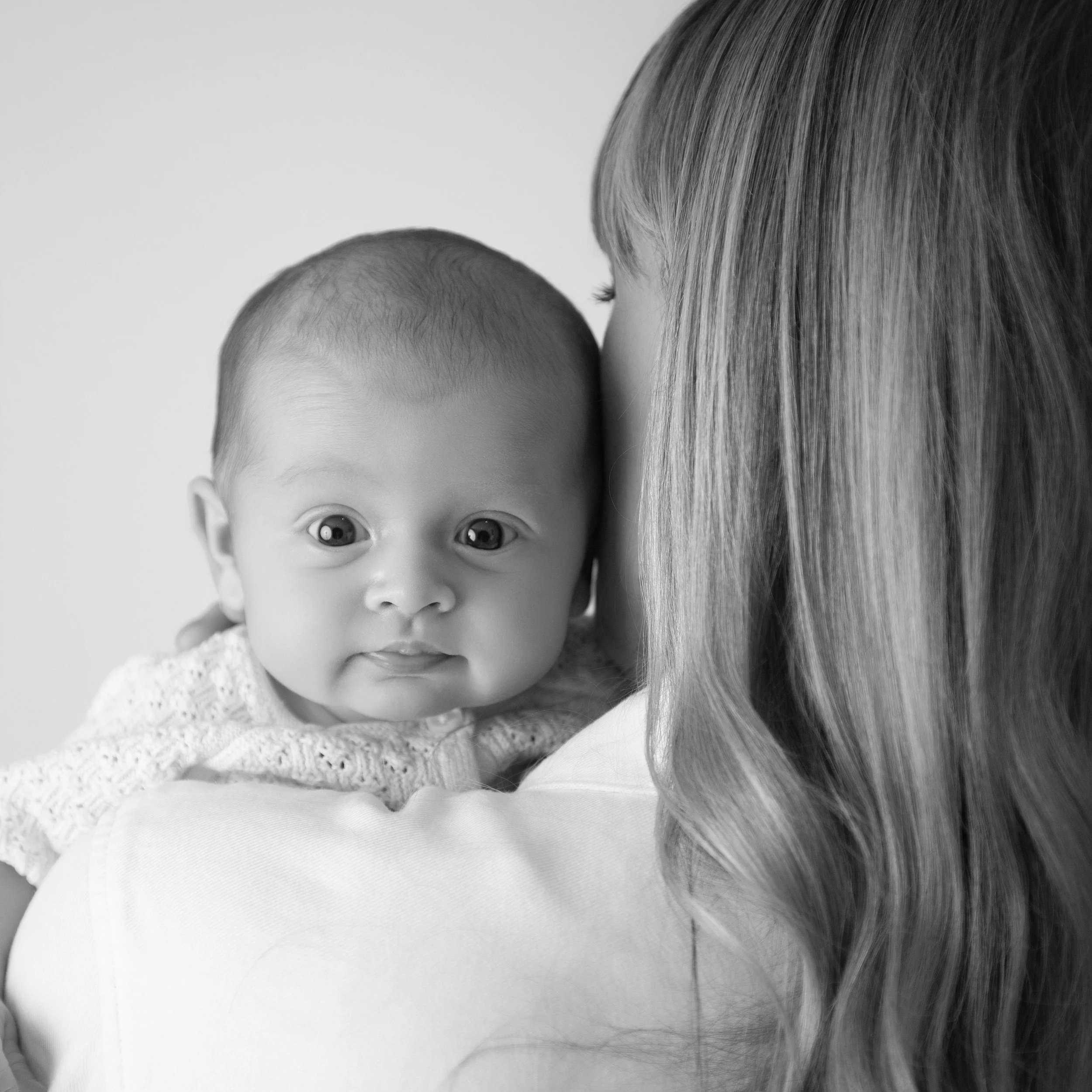 Black and white portrait of a baby looking over a parent's shoulder, newborn photography in Upminster