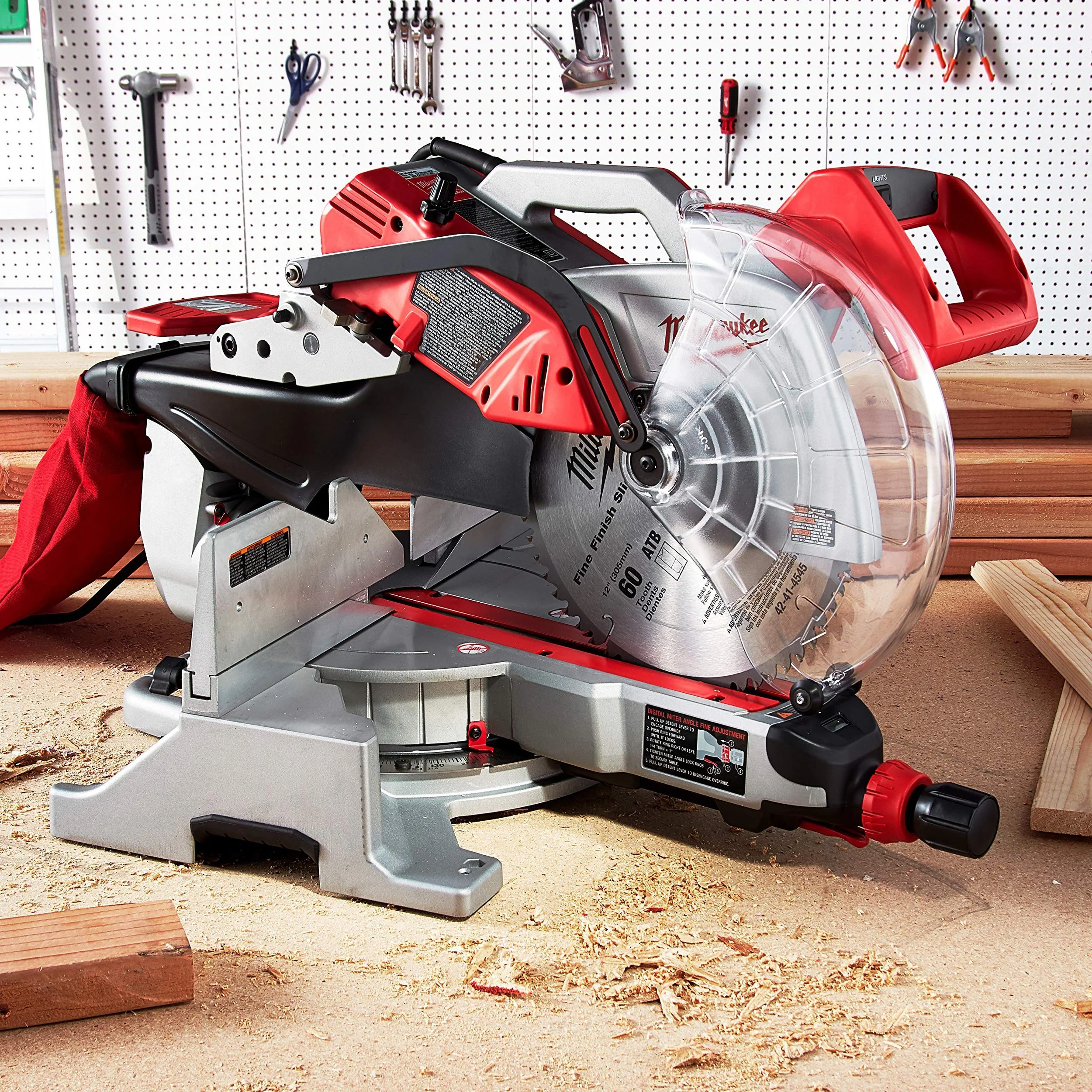 A red and silver miter saw on a wooden workbench in a workshop, with tools hanging on a pegboard behind it.