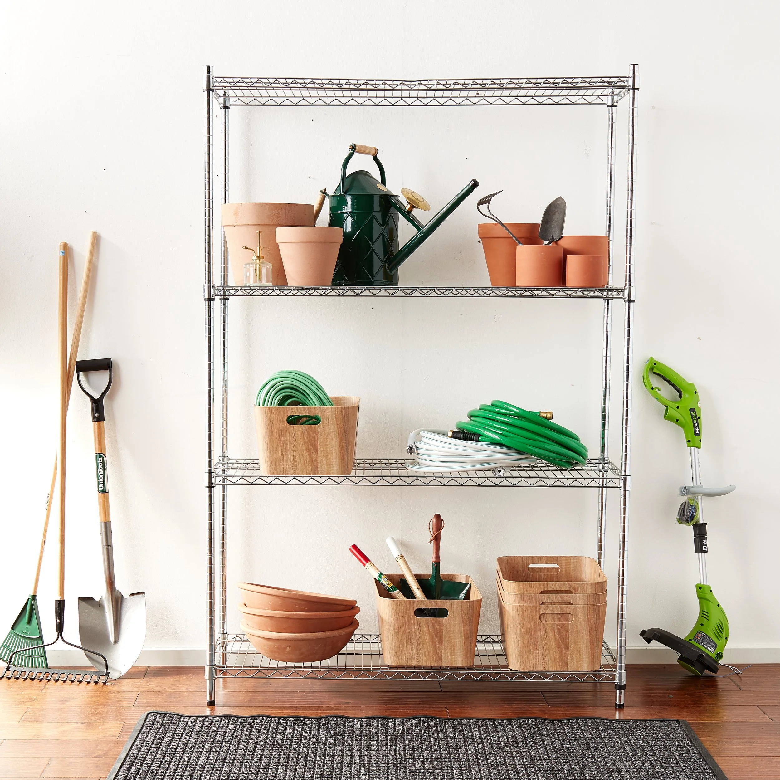 Metal shelving unit with gardening supplies including flower pots, watering can, garden tools, hoses, bowls, and storage containers in a garage or storage room setting.