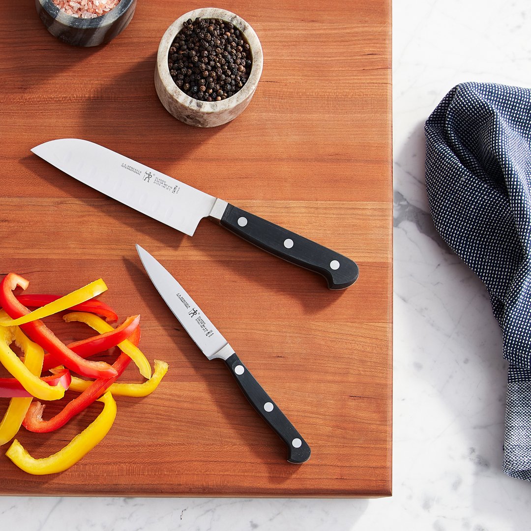Cutting board with sliced yellow and red bell peppers, a large kitchen knife, a smaller paring knife, and bowls of black pepper and pink salt in kitchen setting.