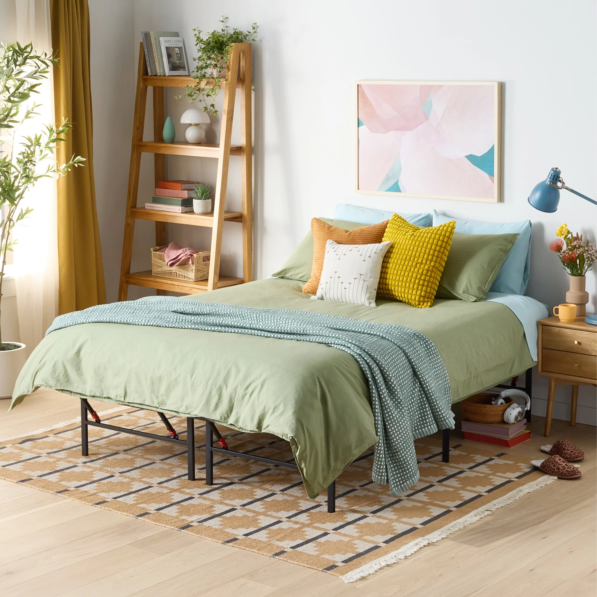 A bedroom with a bed covered in a green duvet, yellow, white, and green pillows. A wooden nightstand with a vase of flowers, a yellow mug, and a blue lamp. A wooden ladder shelf with decorative items and books. A window with yellow curtains, a beige 