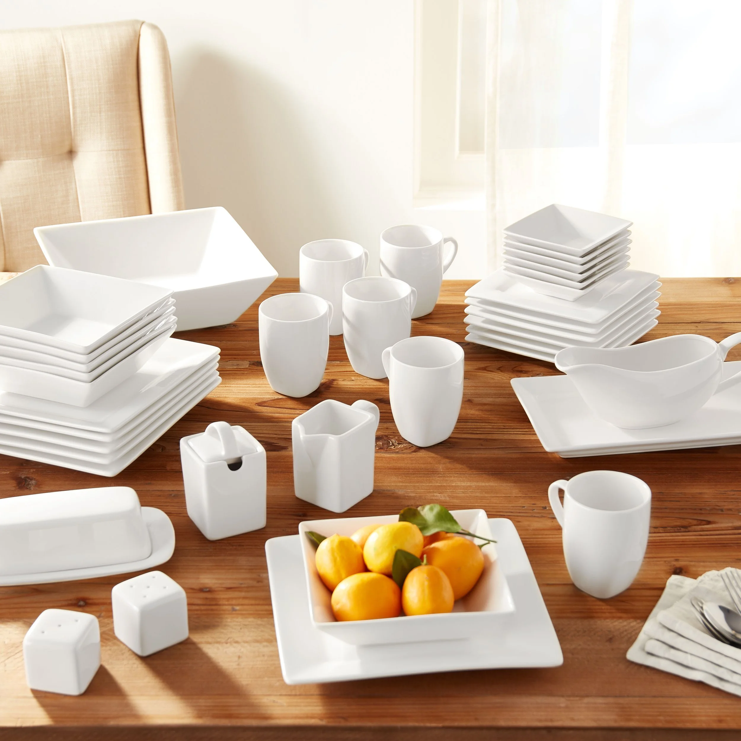 White dinnerware including plates, bowls, cups, and condiment containers arranged on a wooden table with a bowl of lemons in the foreground.