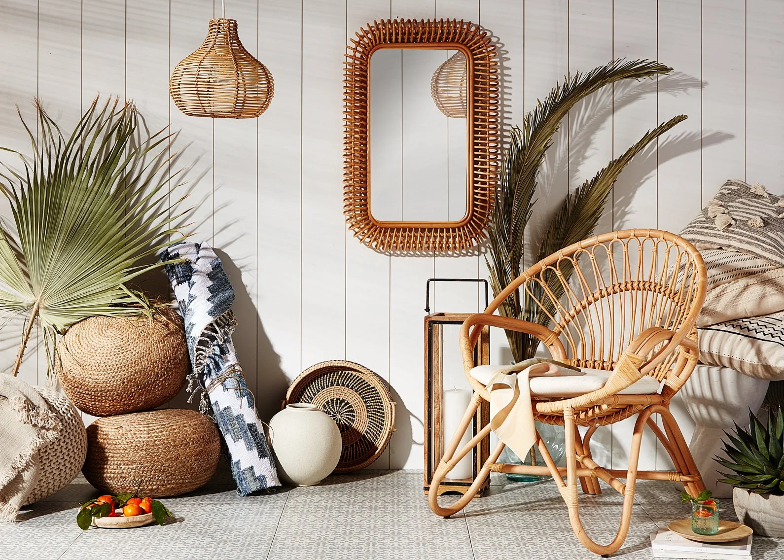 Boho interior with wicker furniture, large green palm leaves, decorative mirror, hanging wicker pendant lights, and cozy textiles.
