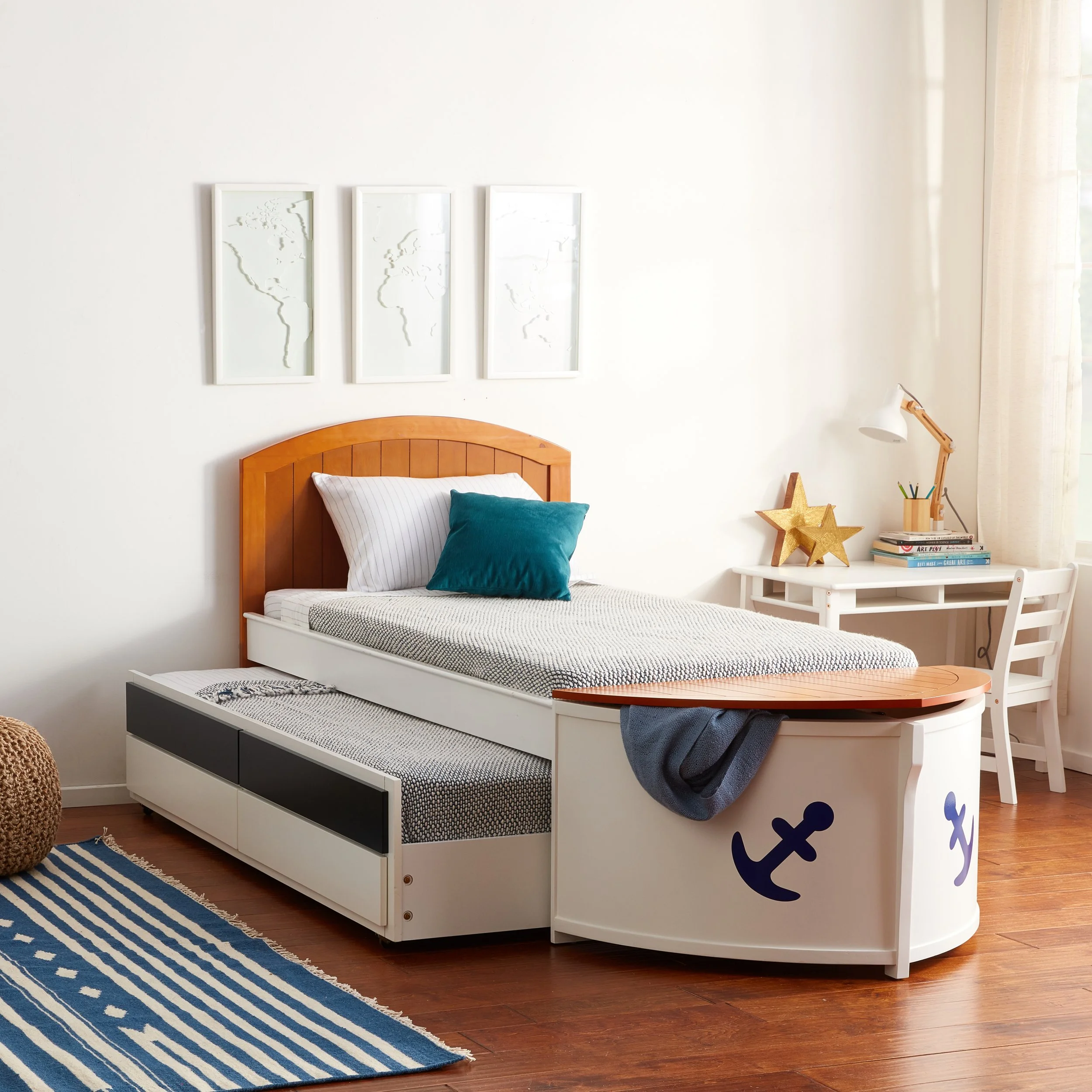 A bedroom with a wooden bed frame, striped bed linens, and pillows, a white desk with gold star decor, and ocean-themed wall art