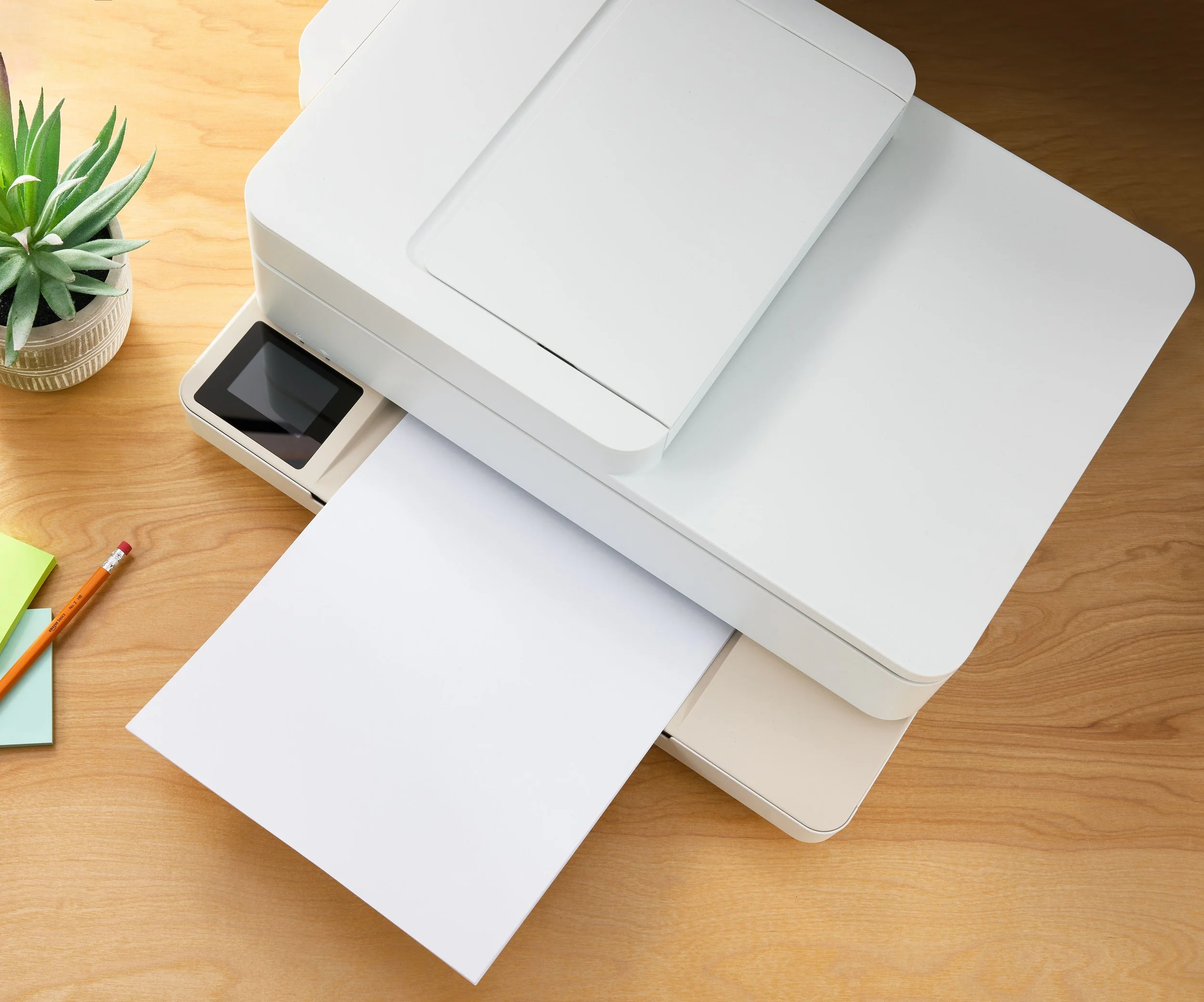 White multifunction printer on a wooden desk with a potted succulent, pencils, and sticky notes nearby