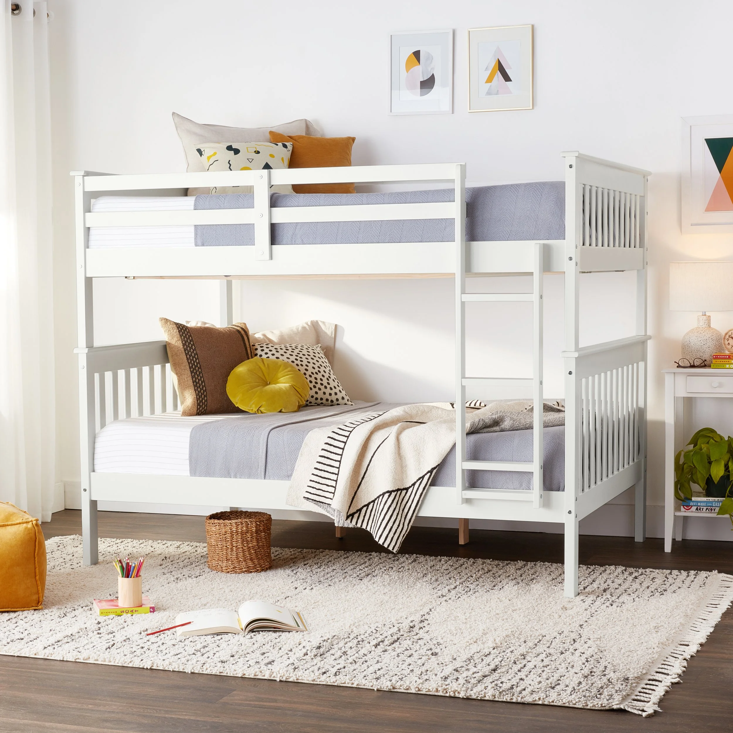 A cozy bedroom with a white bunk bed, decorated with pillows and blankets, a beige rug, and colorful artwork on the wall.