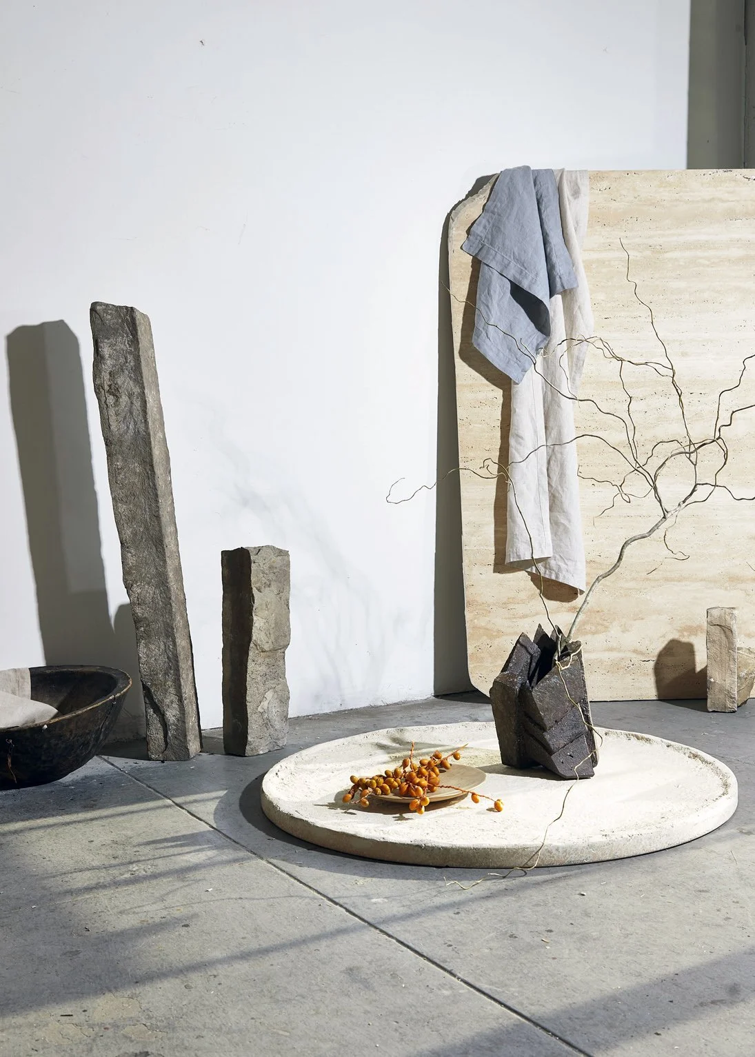 Interior decor with stones, a large round beige rug, draped clothes, and a small branch in a stone vase.