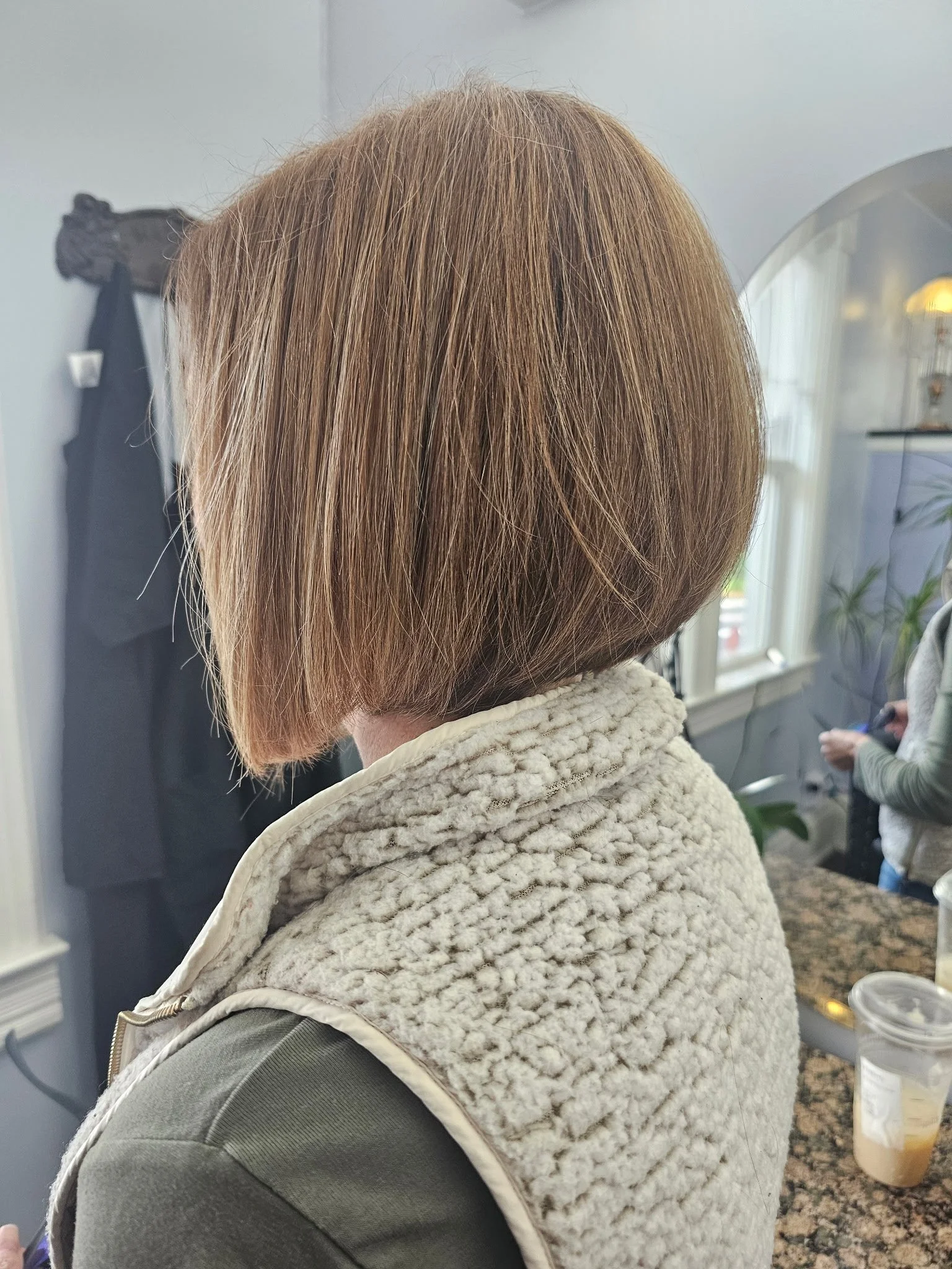 Side view of a woman with short, straight, reddish-brown hair wearing a cream-colored, textured vest in a salon or indoor setting. Radiant Styles by Julie