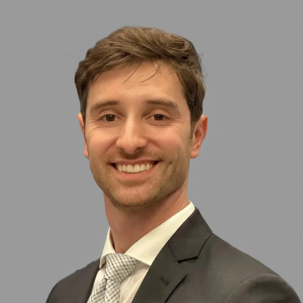 Portrait of a smiling man in a suit and tie against a plain background.