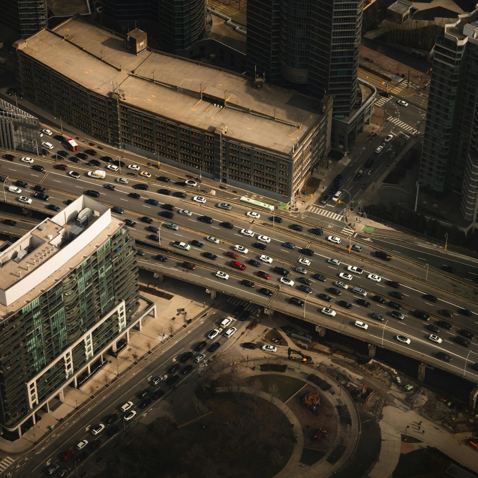 An aerial view of a busy highway with multiple lanes filled with cars in an urban area, surrounded by tall buildings and construction sites.