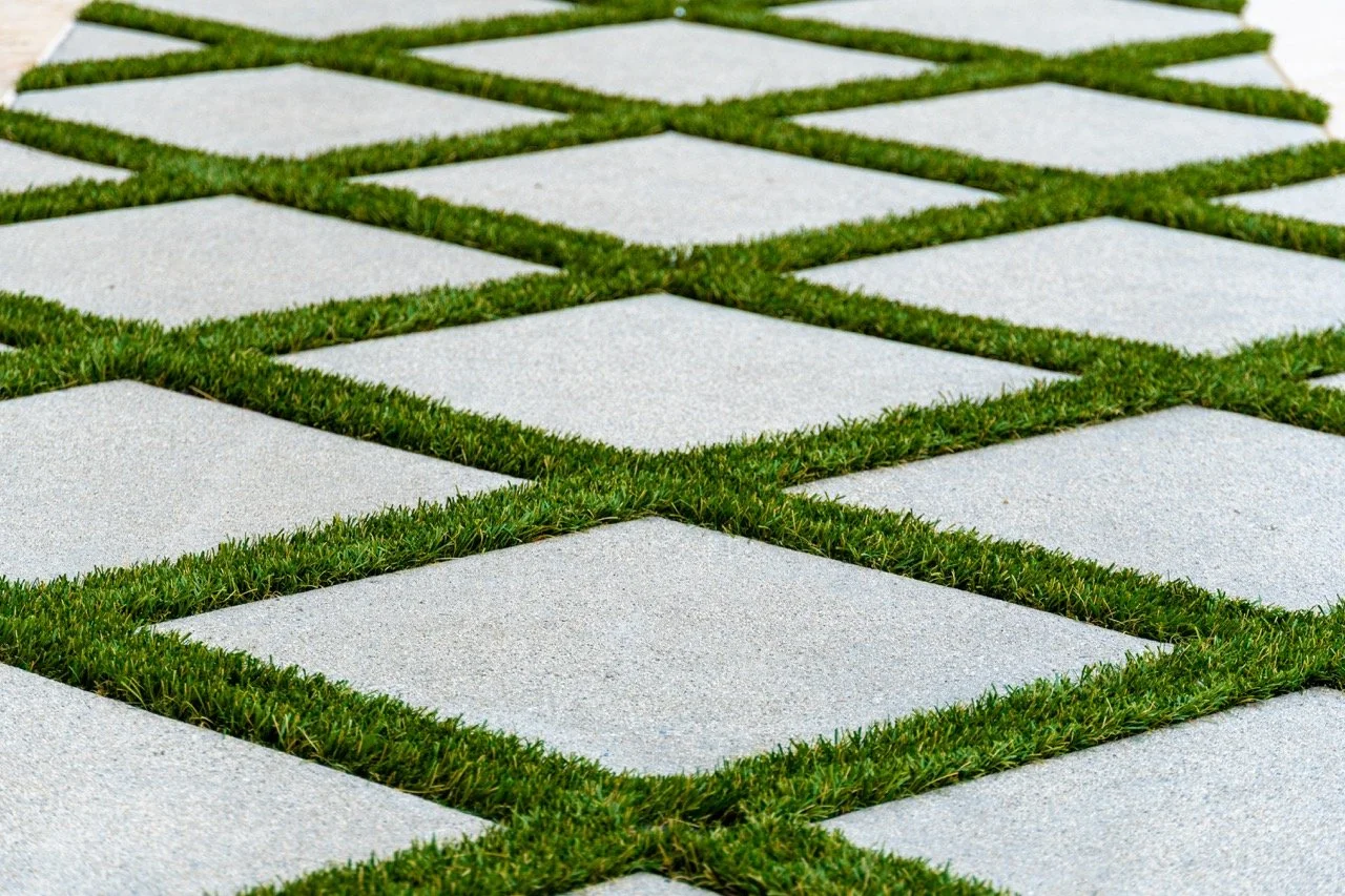 Close-up of a modern pathway with square concrete tiles and green grass growing between the tiles.