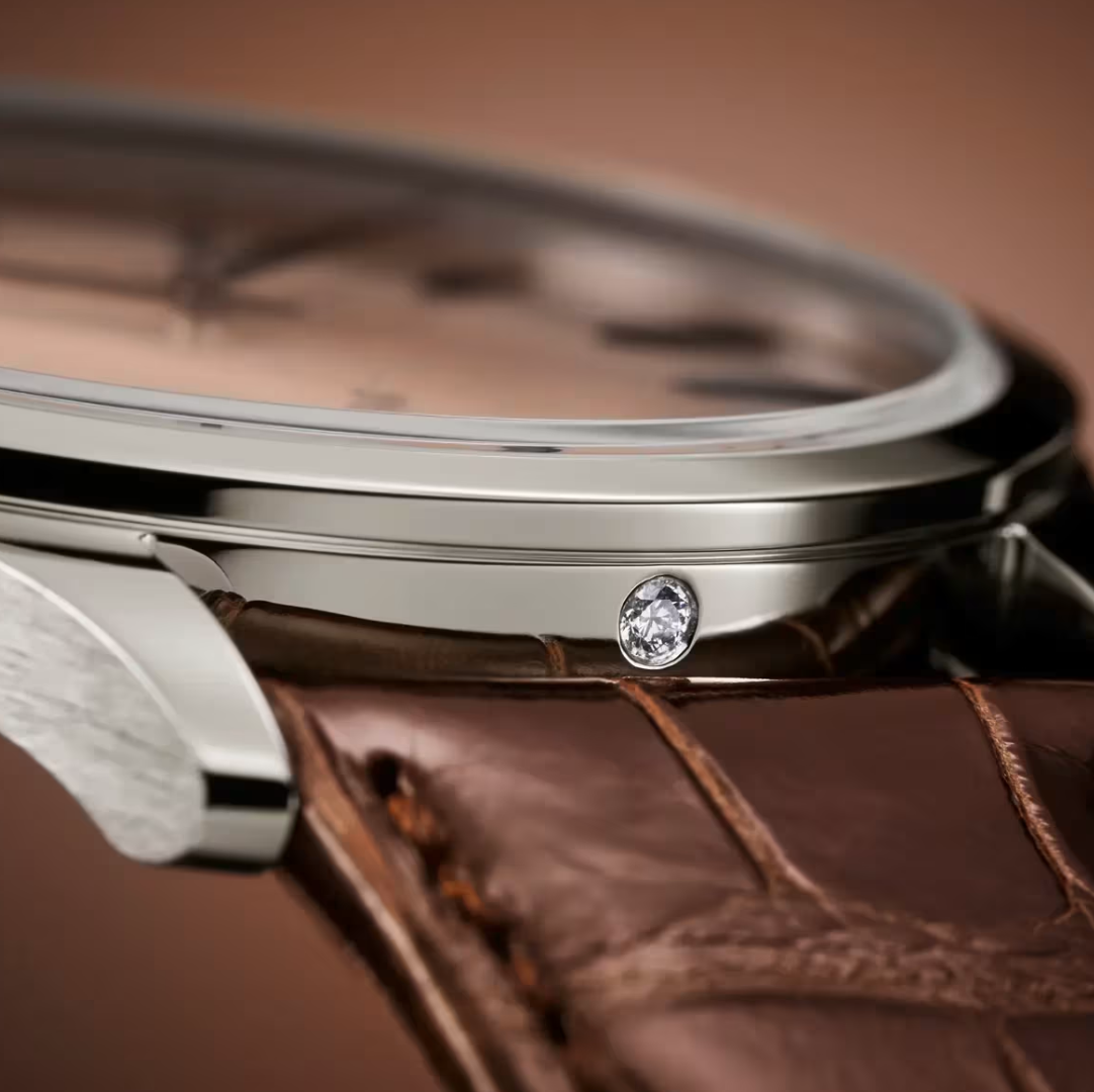 Close-up of a Patek Philippe's platinum case with a brown leather strap, showcasing its iconic diamond embedded on the side.