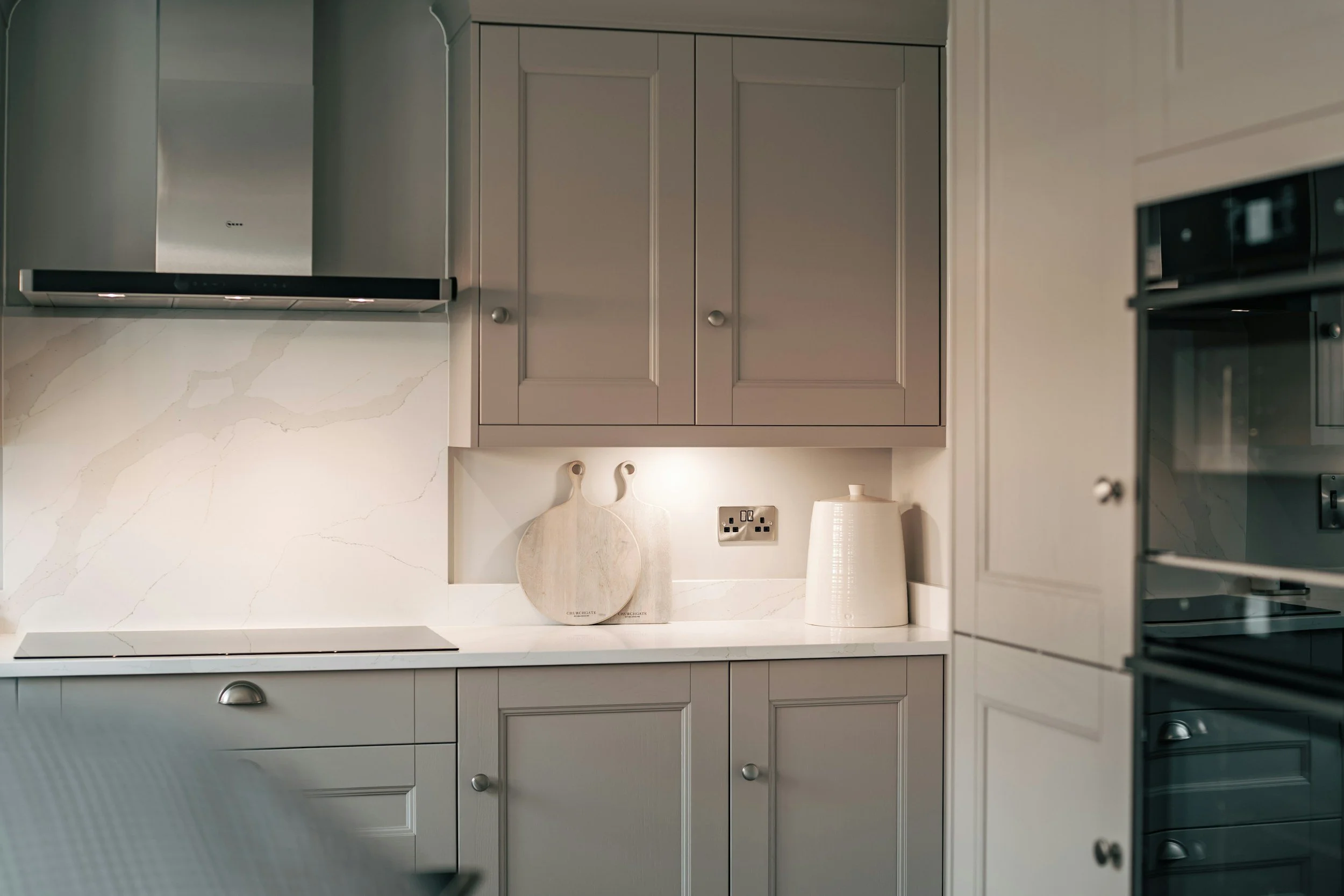 Modern kitchen with grey cabinetry, white marble backsplash, a cooktop, and decorative cutting boards on the countertop.