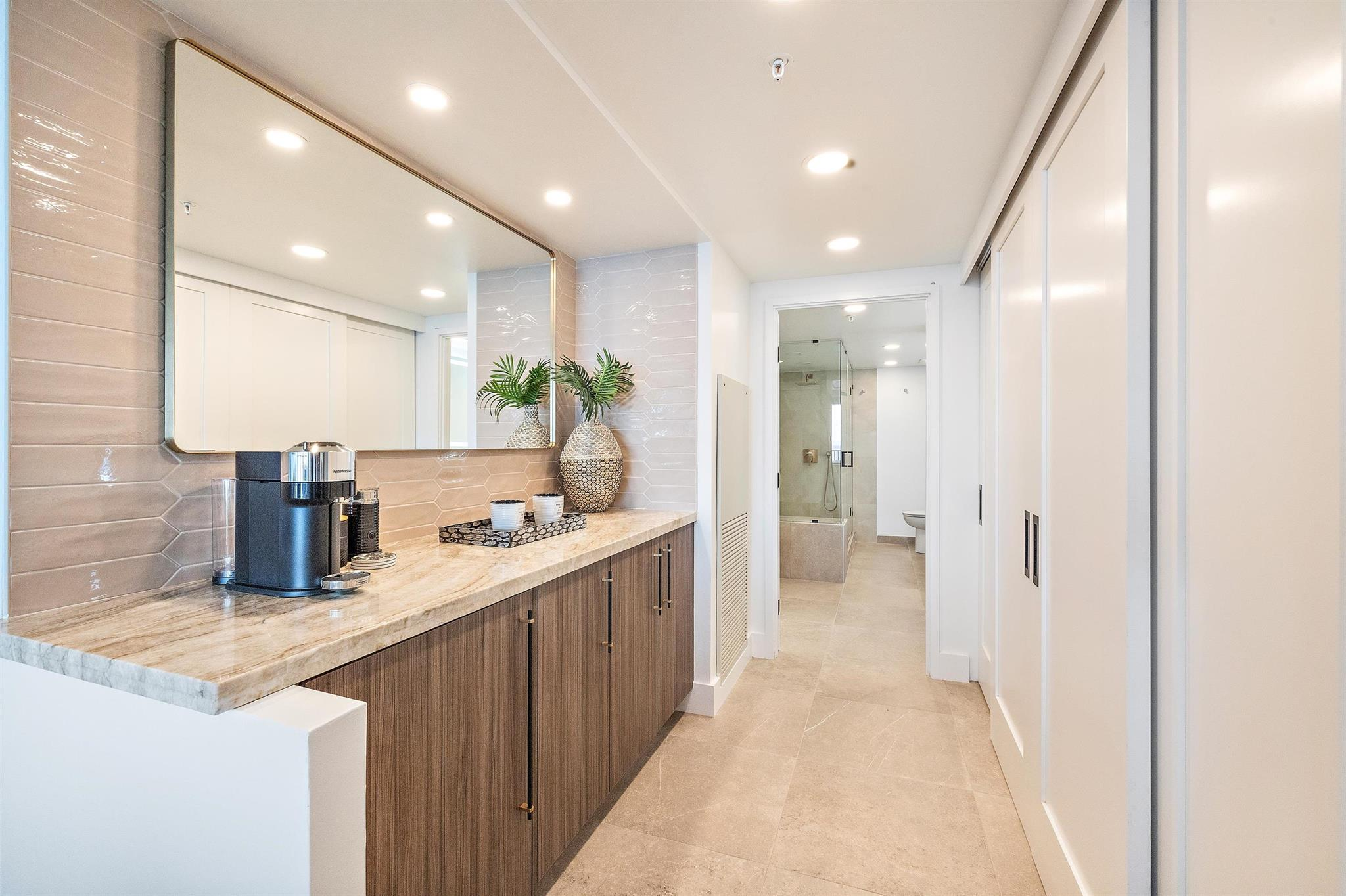Modern bathroom with a marble countertop, decorative vases, and a mirror, leading to a shower and toilet area.