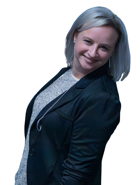Smiling woman with silver hair wearing a dark blazer and a sparkly top, headphones around her neck, posing against a black background.