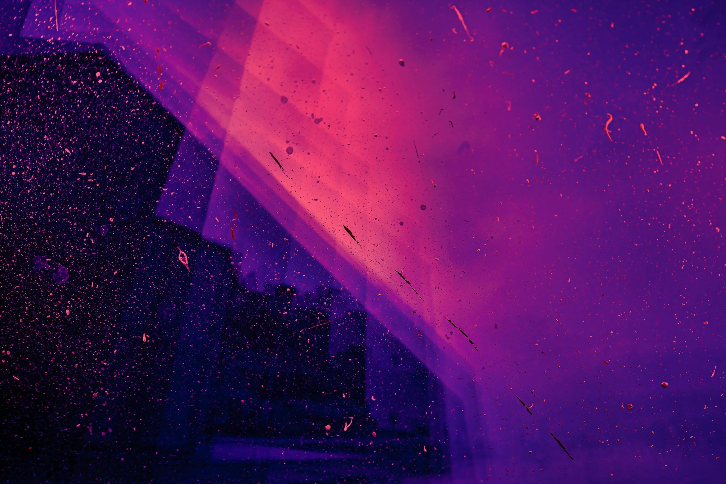 Purple and pink stained glass with dirt and debris on the surface, with silhouettes of buildings visible through the glass.