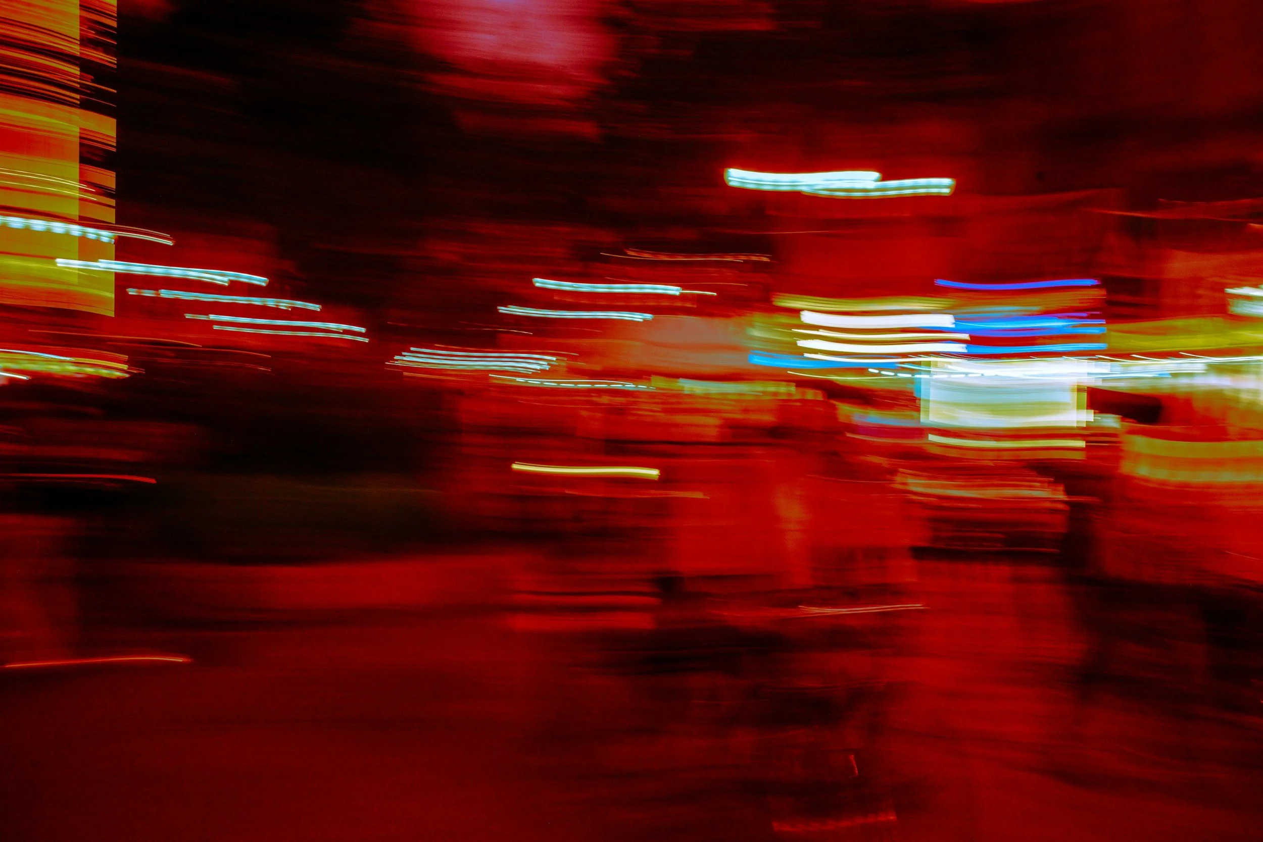 Blurred city street with streaks of red, blue, and yellow lights at night.