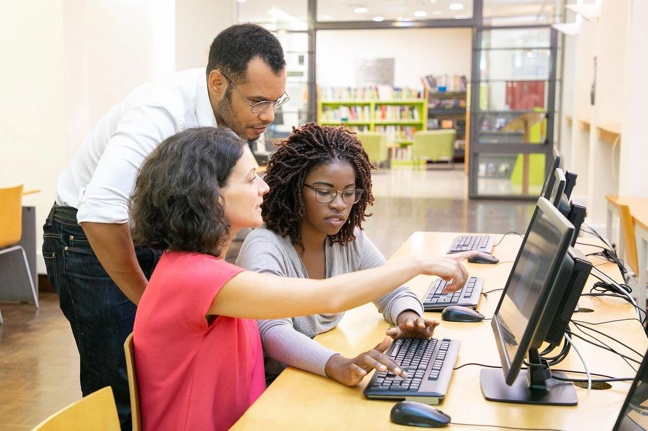 Three people working together at computers in a library or classroom setting