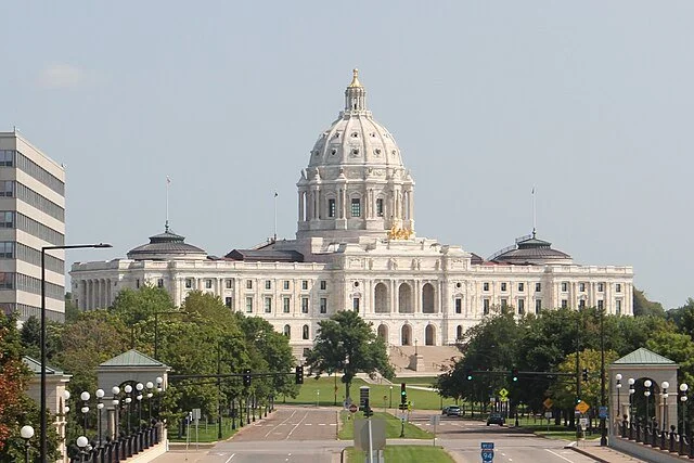 Capitol building with a large dome, trees, and a paved walkway in front
