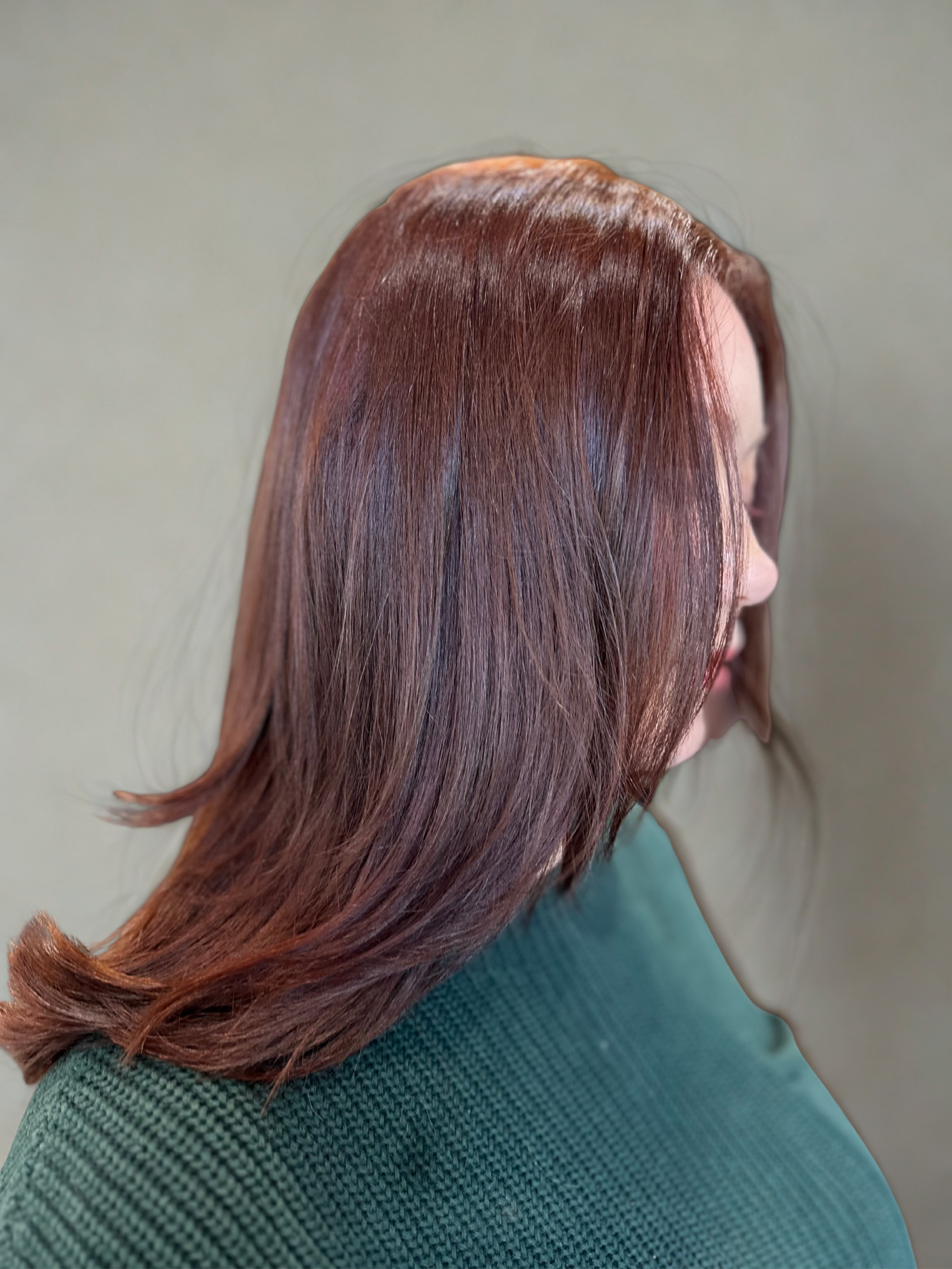 Side view of a woman with shoulder-length auburn copper hair, wearing a green sweater.