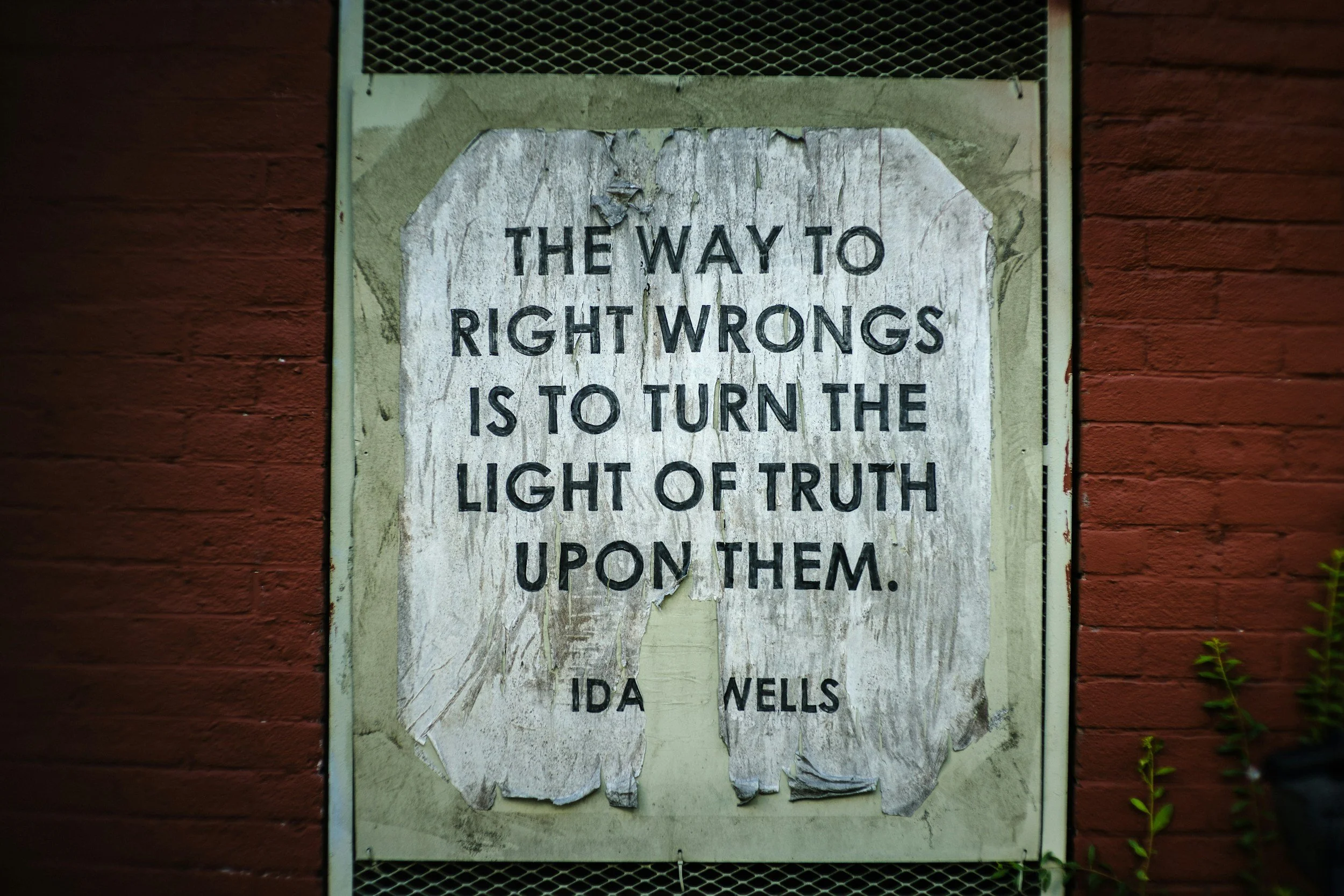 Old, weathered sign on a brick wall that reads: "The way to right wrongs is to turn the light of truth upon them."