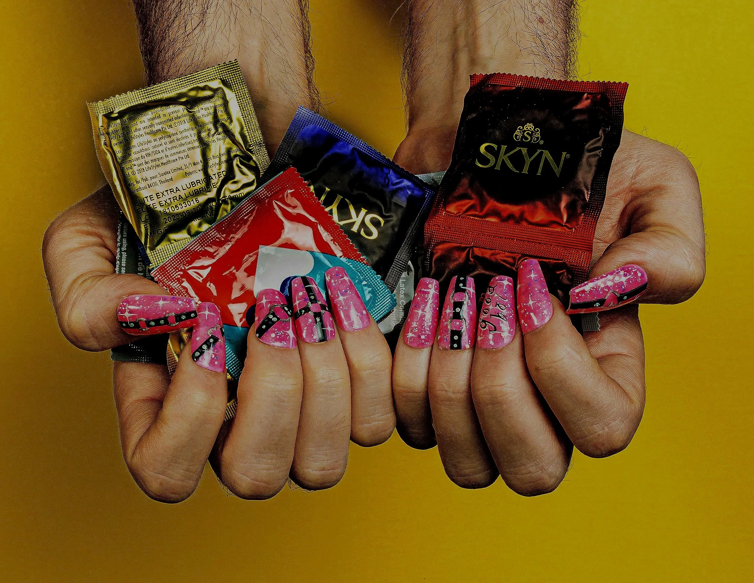 Hands with long colourful nails holding an assortment of condoms