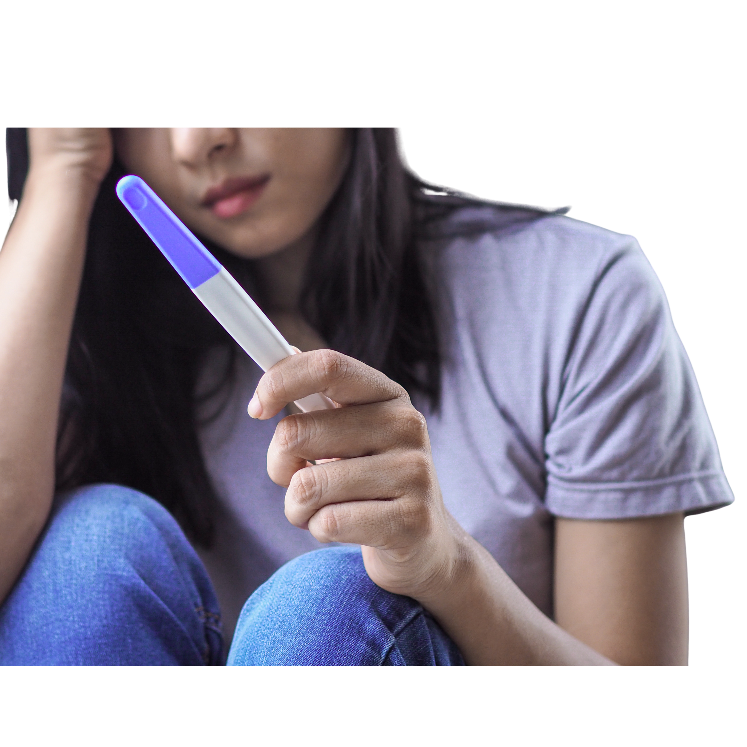 Female sitting alone with knees pulled up to chest holding a pregnancy test