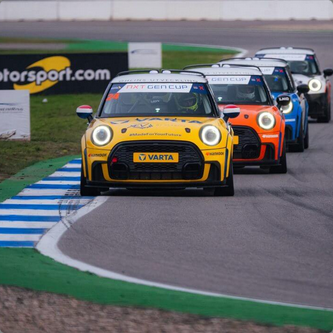 A group of race cars, including a yellow Mini Cooper, on a race track during a race.