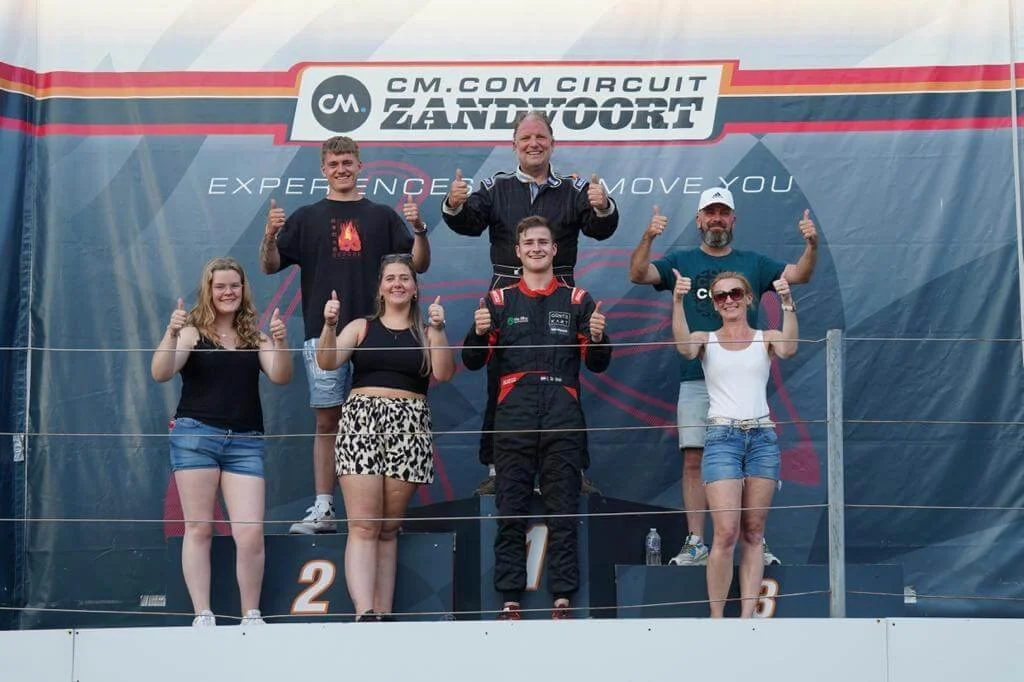 Podium ceremony at CM.com Circuit Zandvoort with smiling racers and supporters giving thumbs up, celebrating their victory.