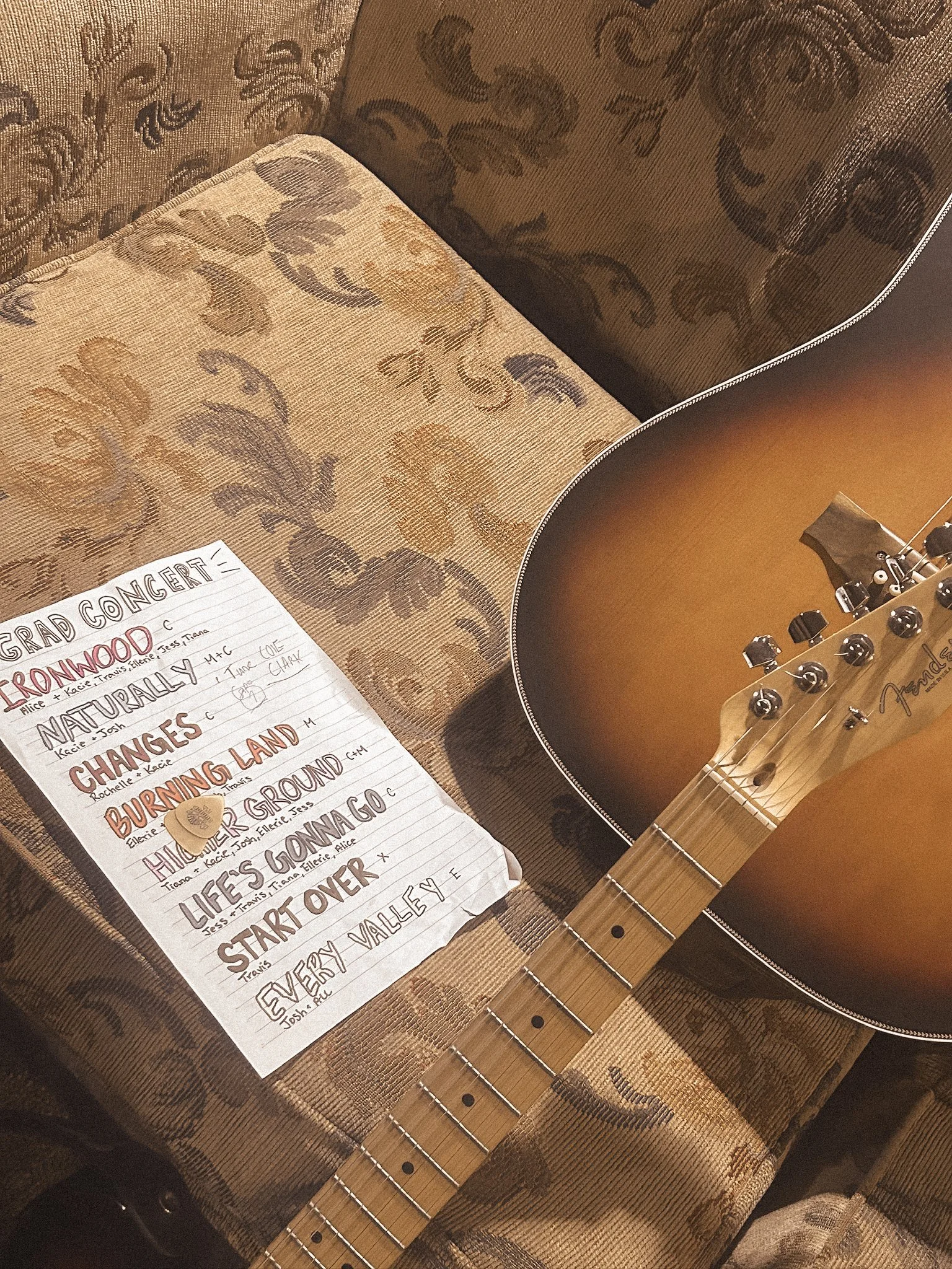 Close-up view of an acoustic guitar resting on a fabric surface, with a handwritten setlist on lined paper nearby.