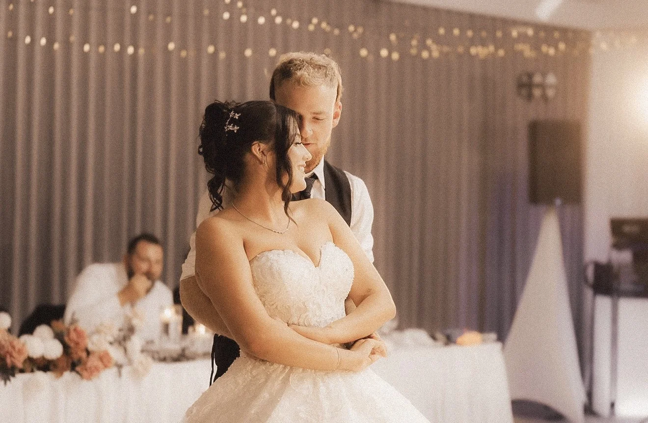 A bride and groom dancing at their wedding reception with guests and decorations in the background.