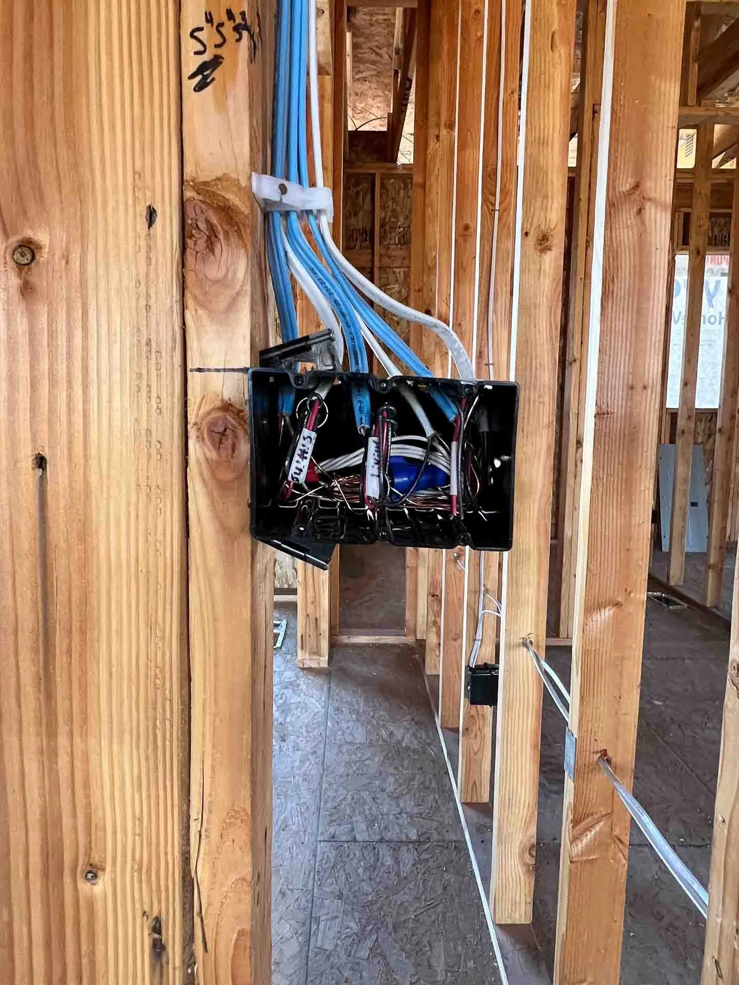 Electrical wiring box with blue, white, and black wires inside a wood-framed building under construction.