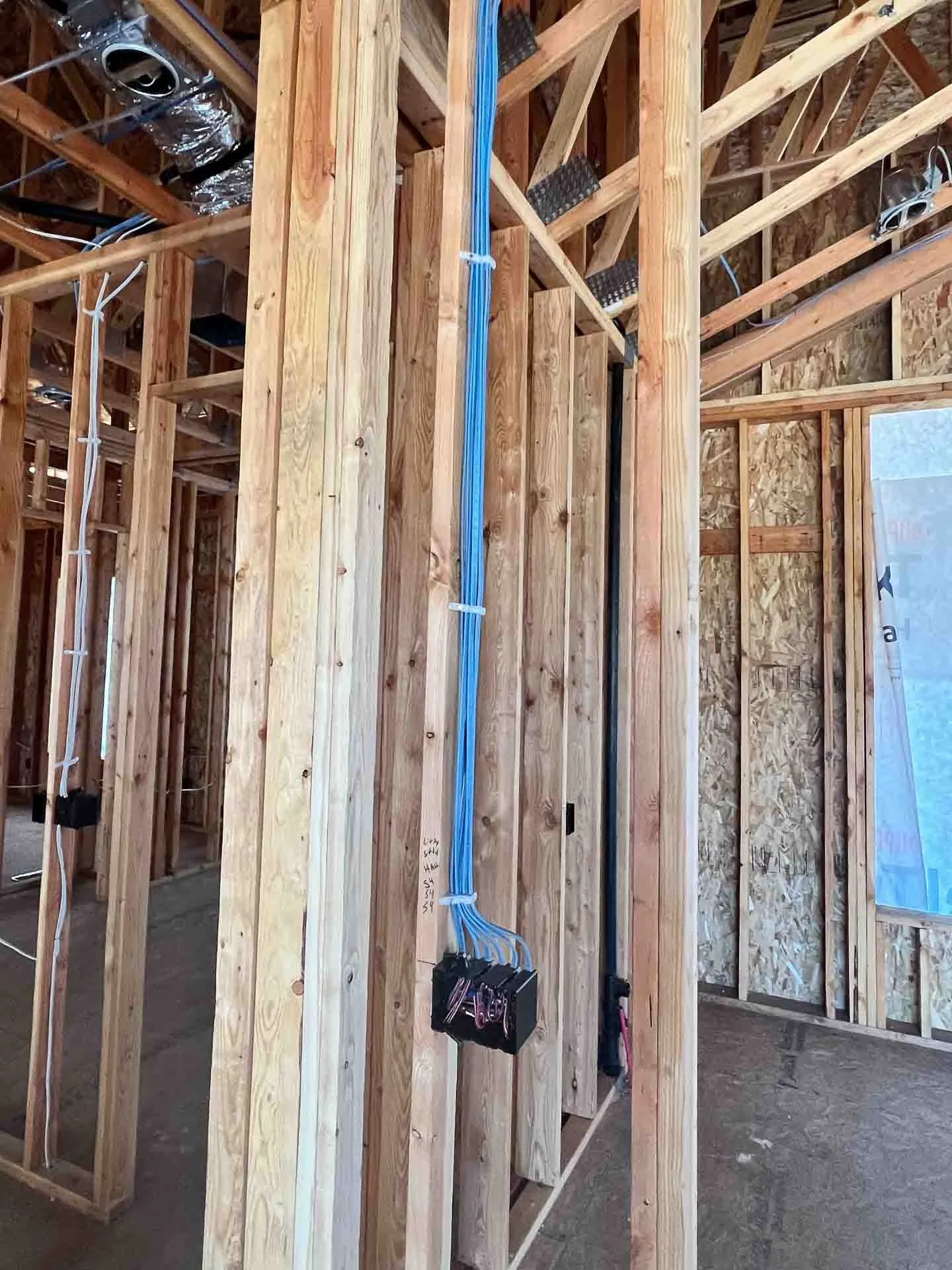 An unfinished interior of a house under construction showing wooden framing, electrical wiring, and blue electrical conduits installed in the walls.