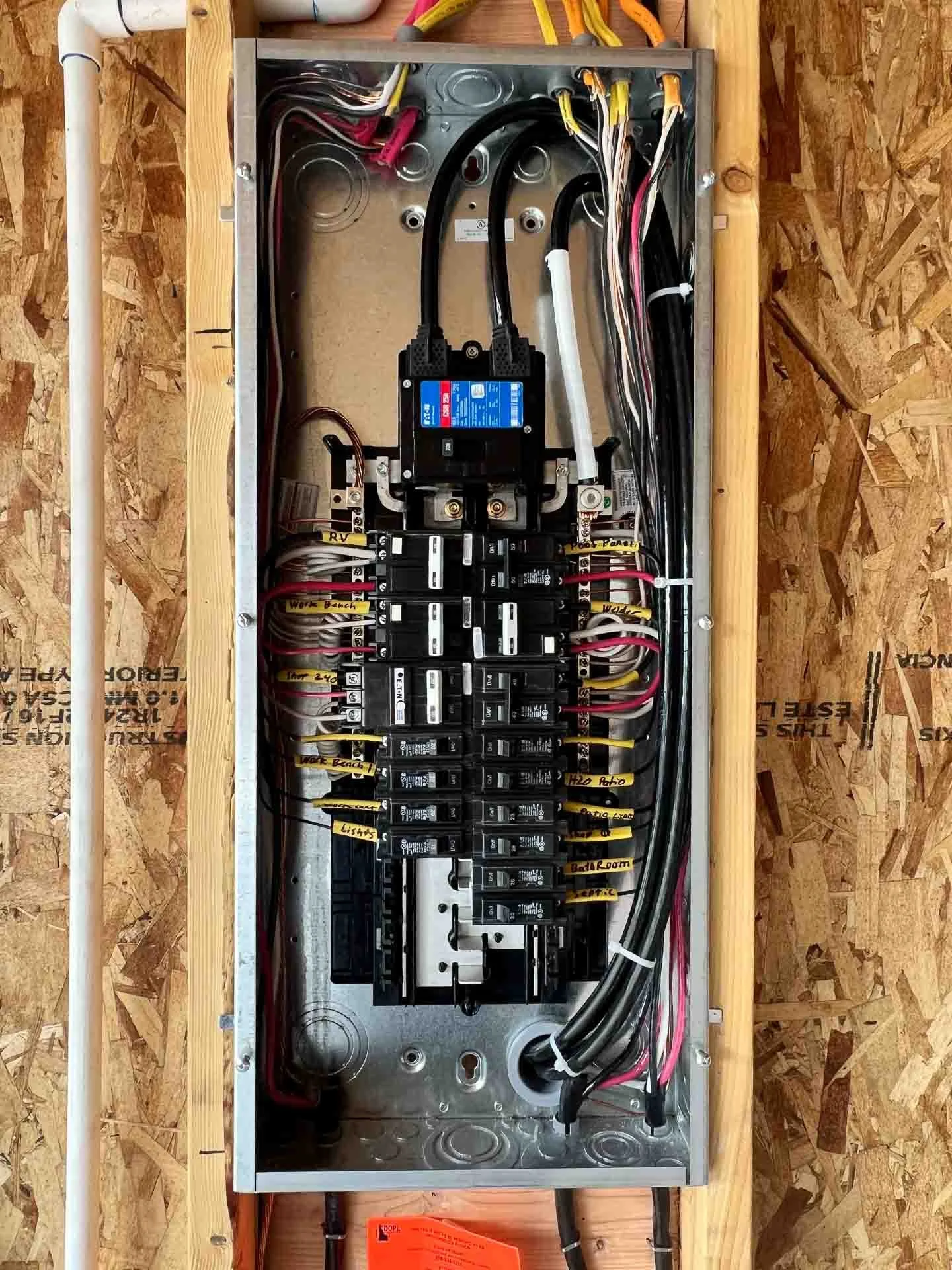 Inside an electrical panel with labeled circuit breakers, wiring, and a disconnect switch on a wooden wall.