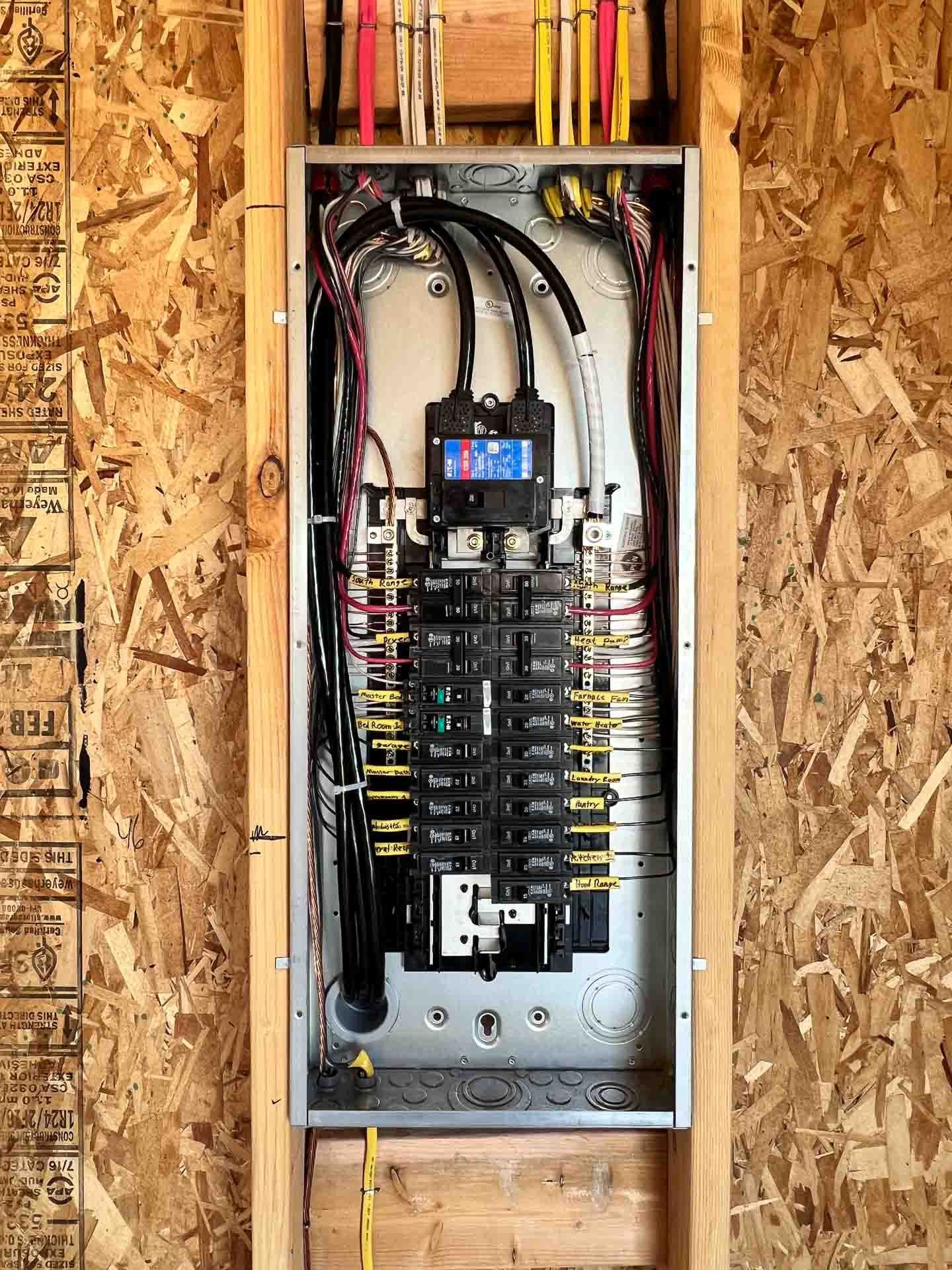 Electrical breaker box with multiple circuit breakers and wiring inside a wooden frame.