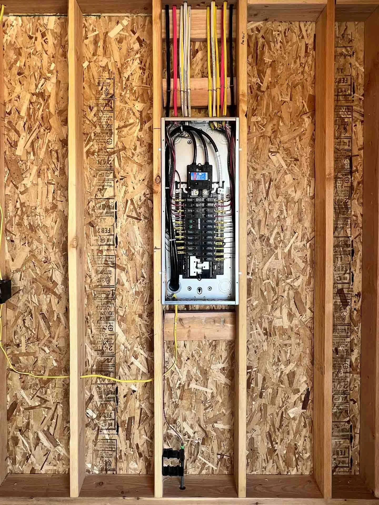 Electrical panel and wiring inside a framed wall with wooden studs and OSB sheathing.