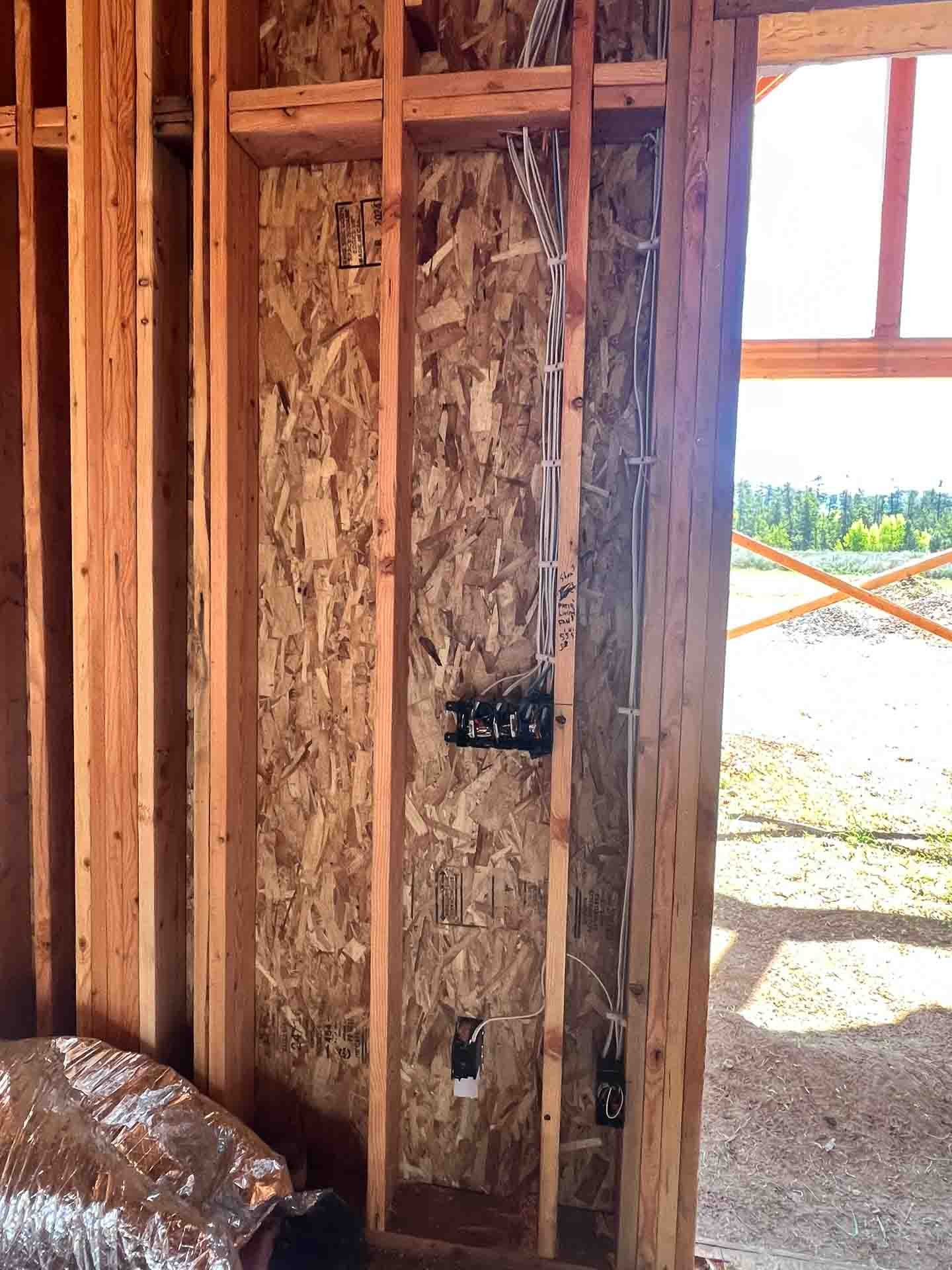 Electrical wiring and breaker box installed on a wooden wall in a building under construction.