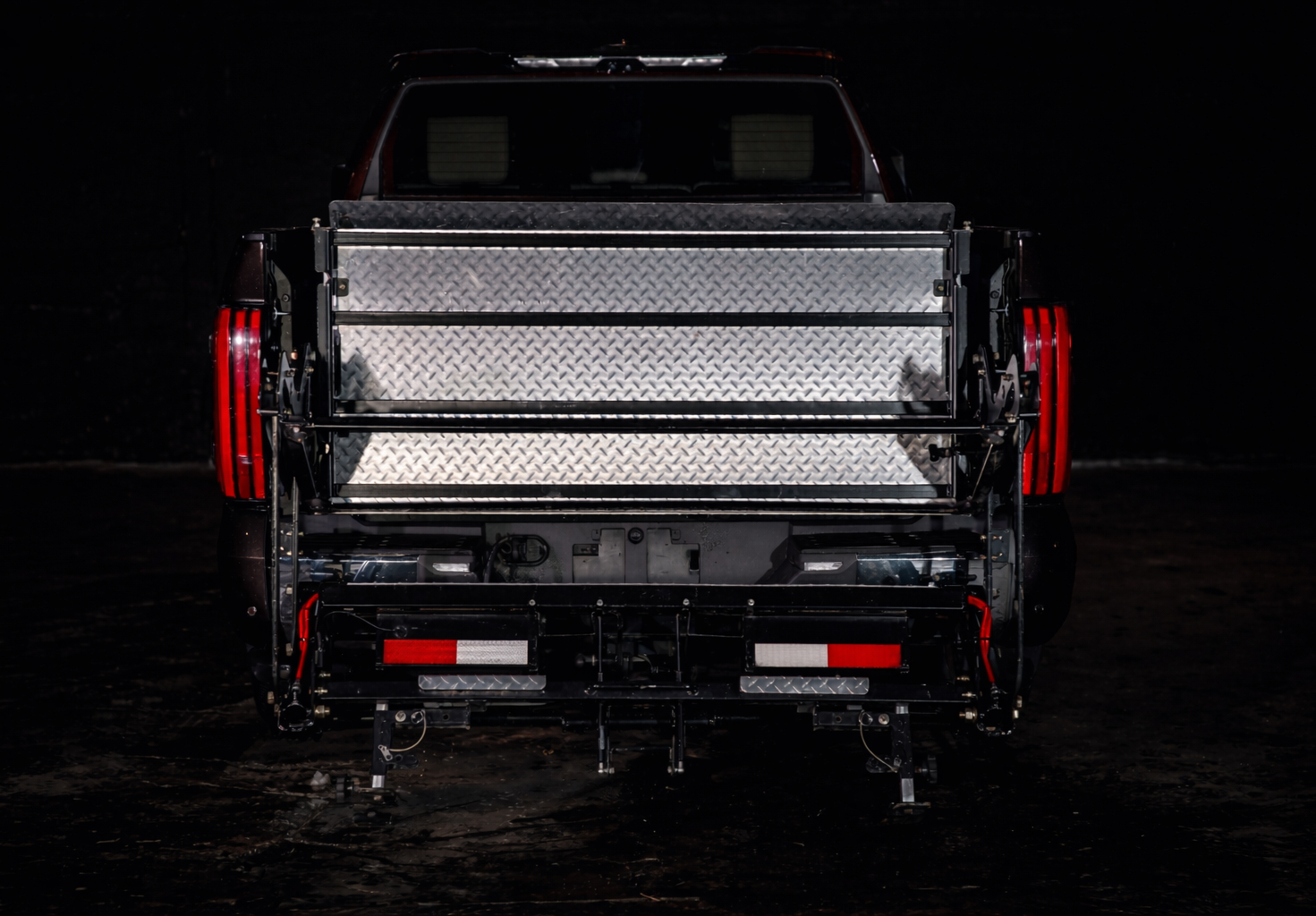 Rear view of a black pickup truck with an empty cargo bed and the ProLiftgate attached, parked in a dark area.