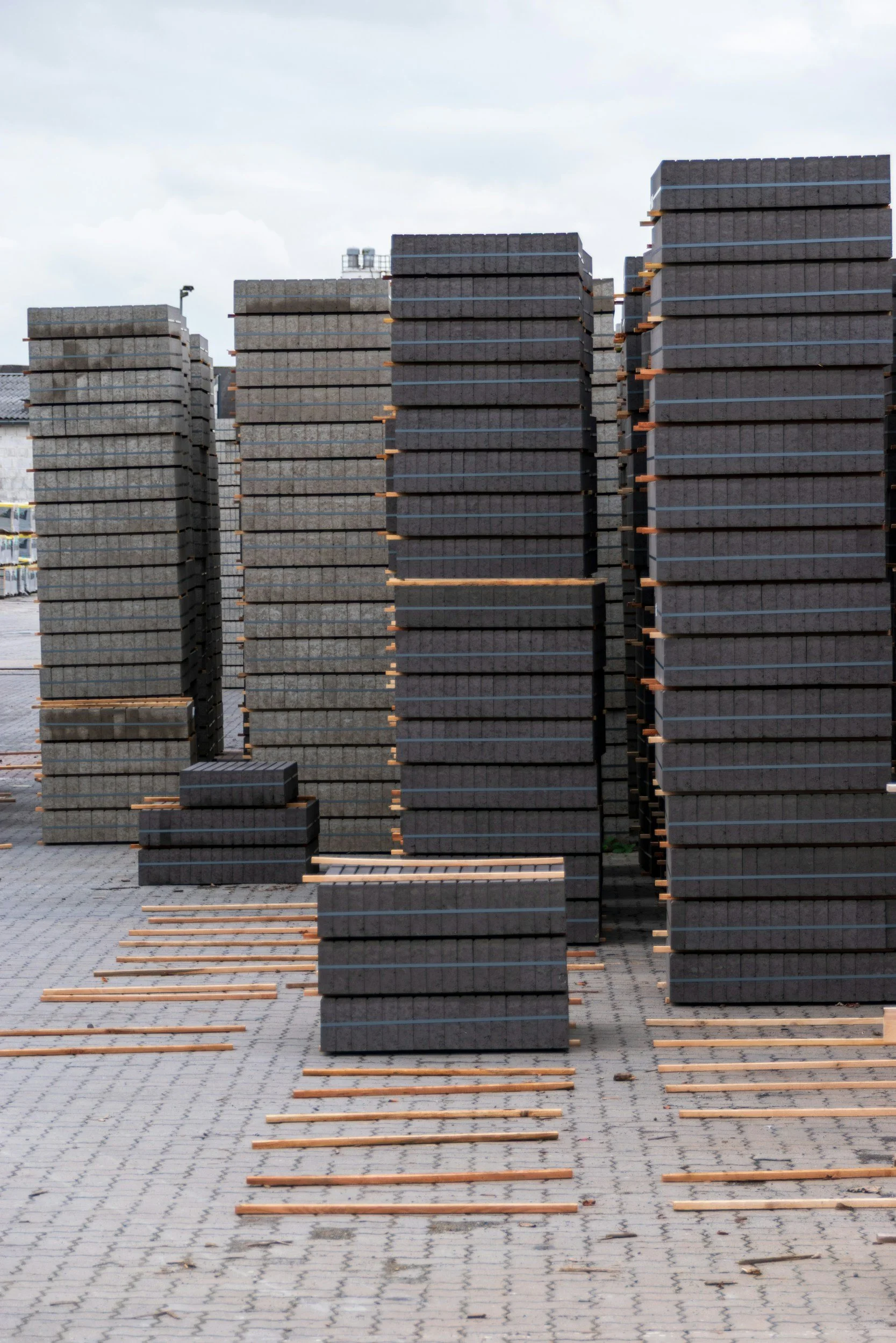Stacks of black paving stones arranged on wooden pallets in an outdoor storage area.