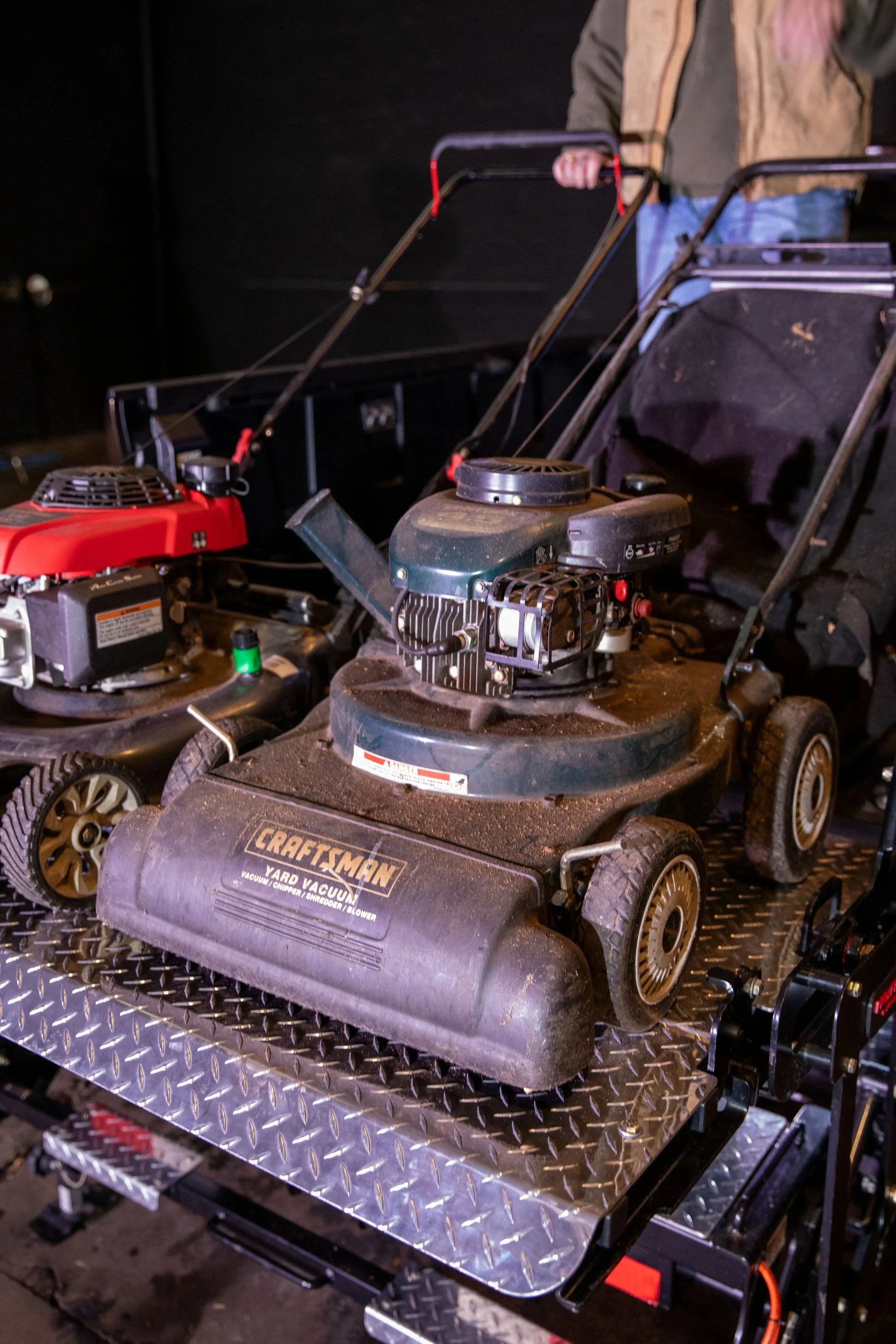 A lawnmower and blower on the ProLiftgate, with a gas-powered engine, small wheels, and dust on the surface.