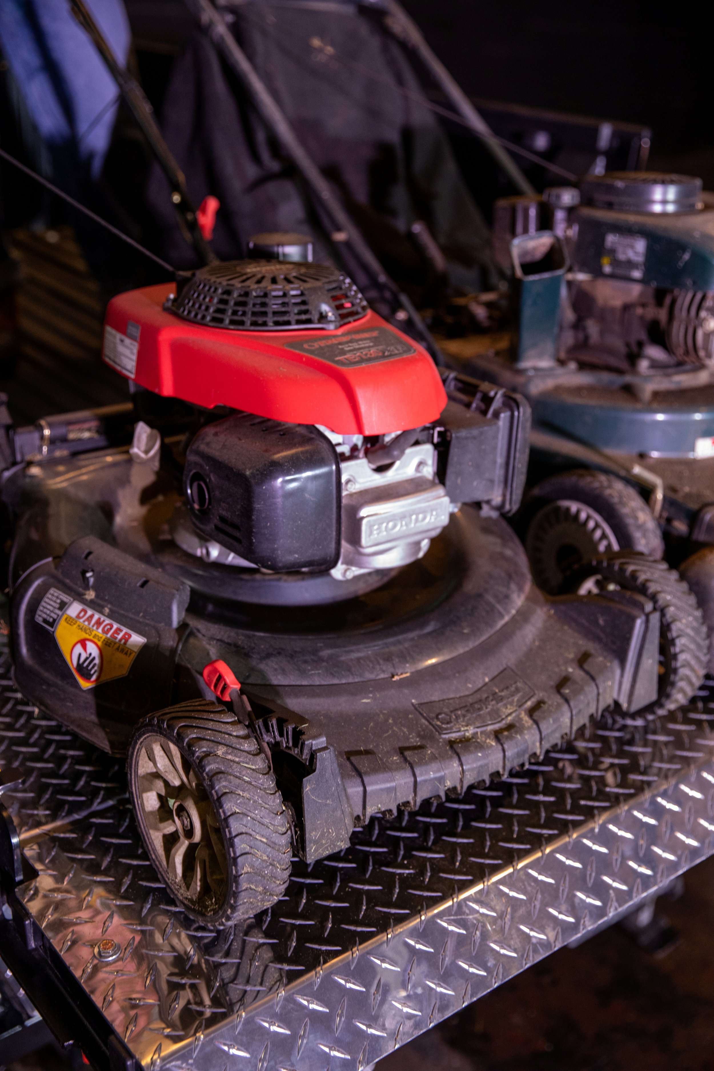 A lawn mower with a red engine cover, black wheels, and a warning sticker on the side, placed on the ProLiftgate.