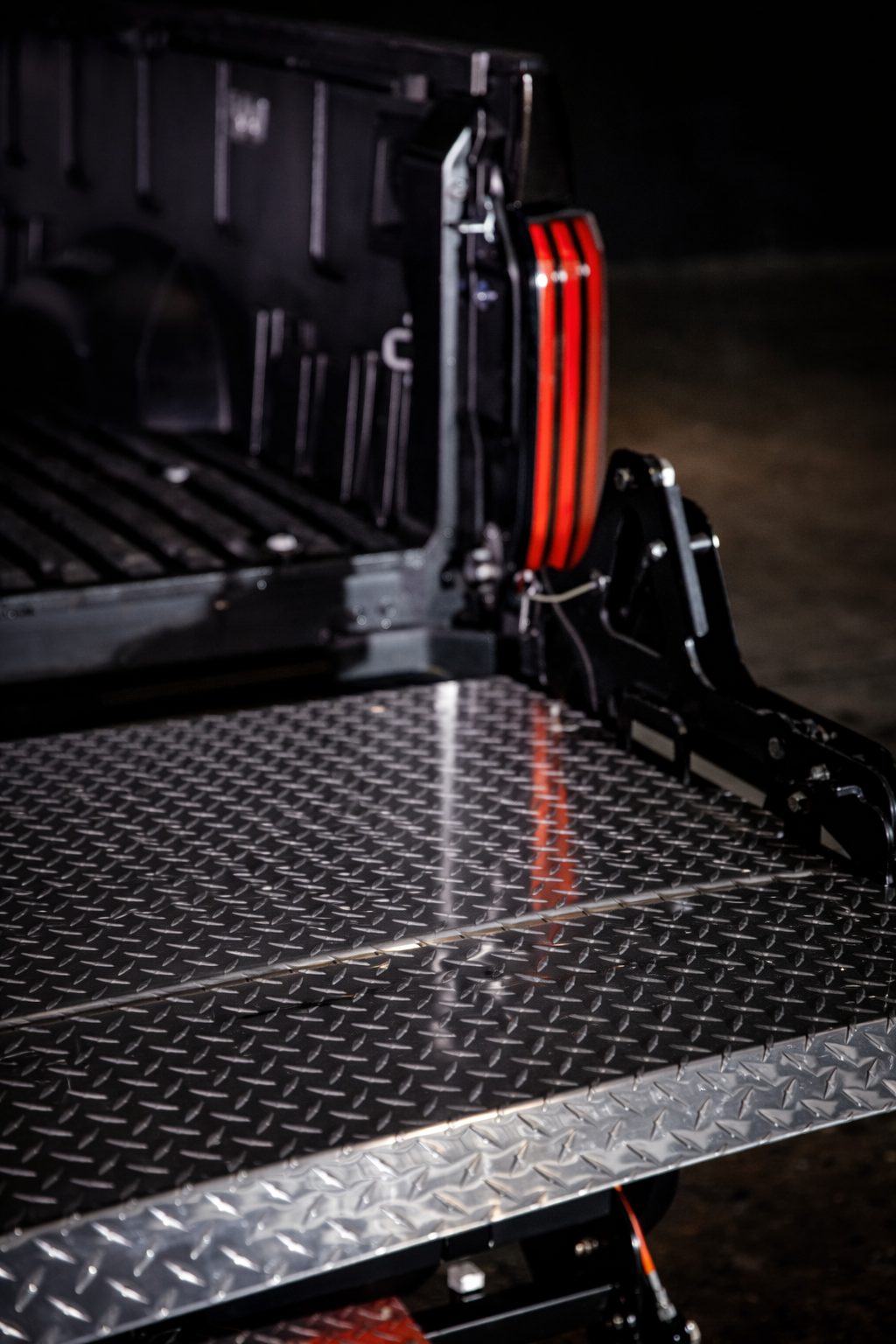 Close-up of a truck bed with ProLiftgate attached, showing part of a black vehicle rear with a red taillight.