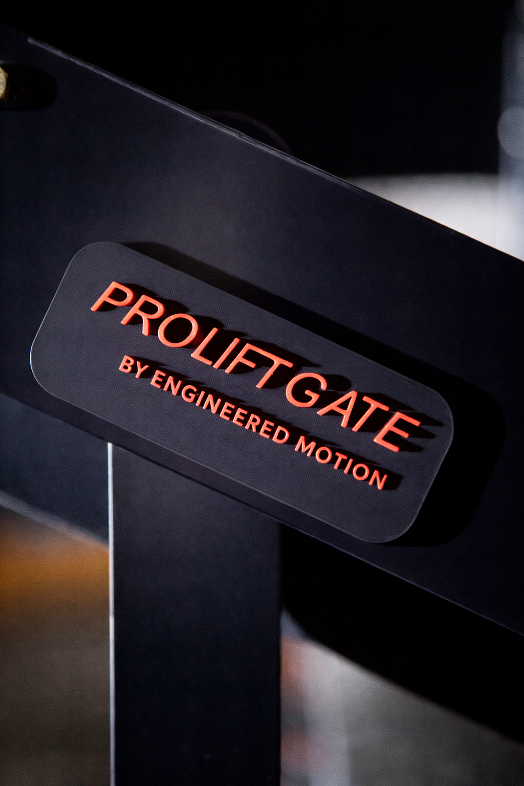 Close-up of a black security gate with the words 'ProLiftgate' in red letters and 'by engineered motion' in smaller red letters underneath.