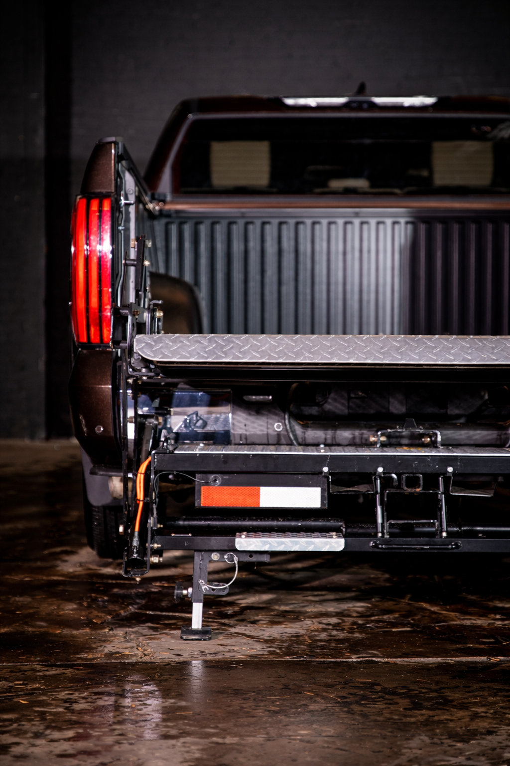 The rear of a pickup truck showing the tailgate and taillight, with the tailgate open, a black bed liner visible, and ProLiftgate attached.