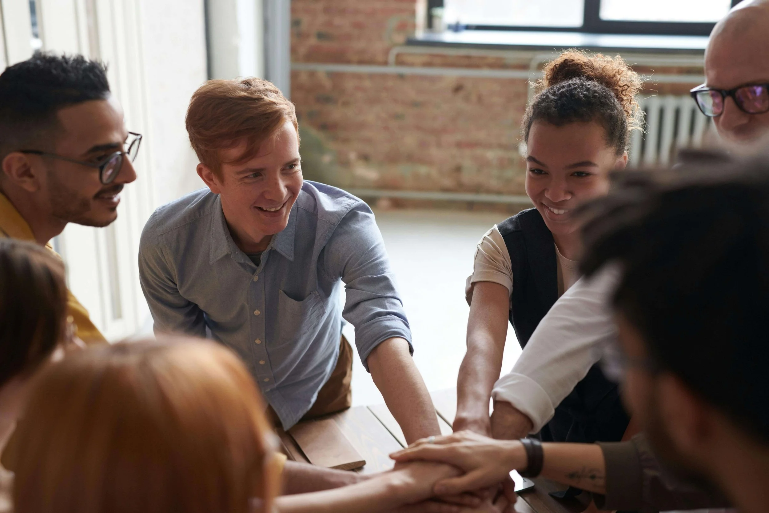 Diverse group of adults smiling and joining their hands together during a collaborative team meeting.