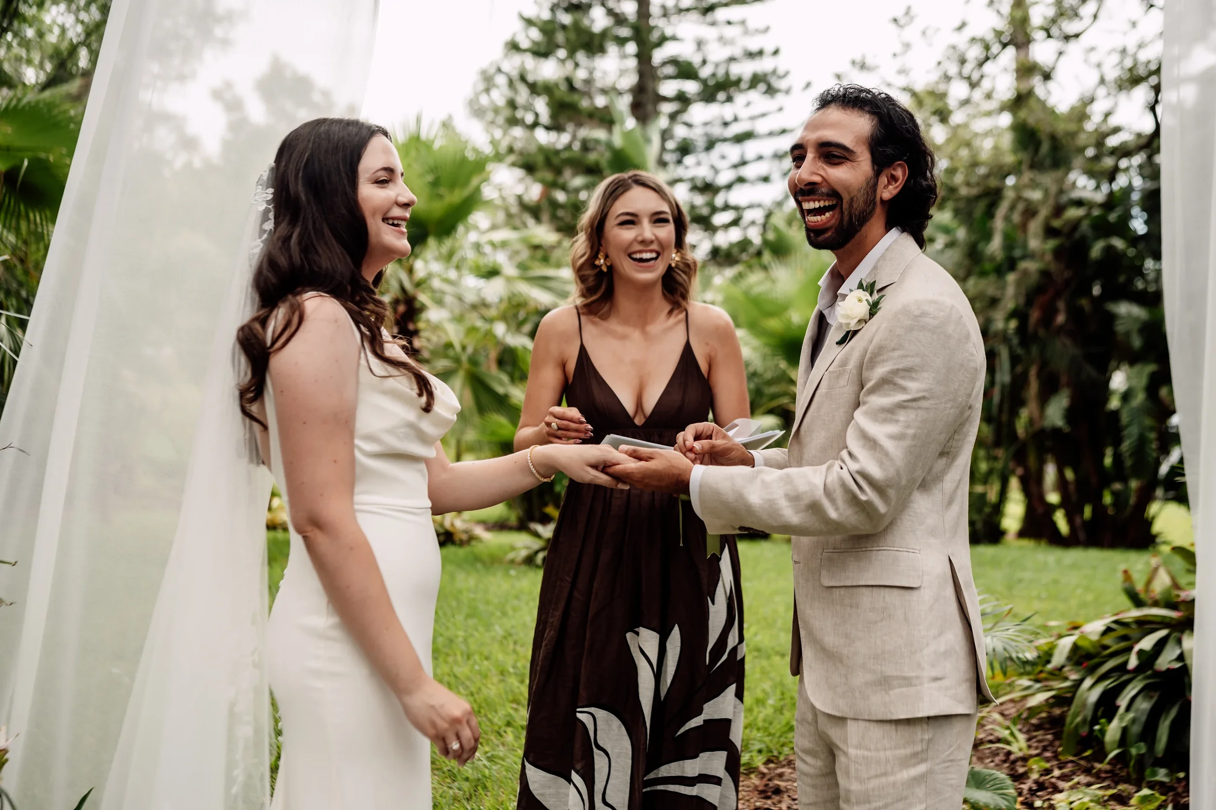 A couple getting married outdoors with two women, one officiating, in a lush garden setting.