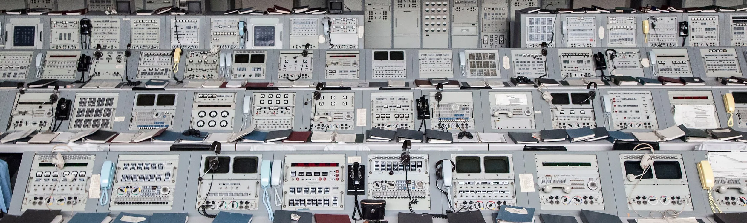 A large wall of vintage airplane cockpit control panels and instruments with various dials, switches, and screens, some with hand-held communication devices indicating all of the logistics necessary to produce a brand film for a space company.