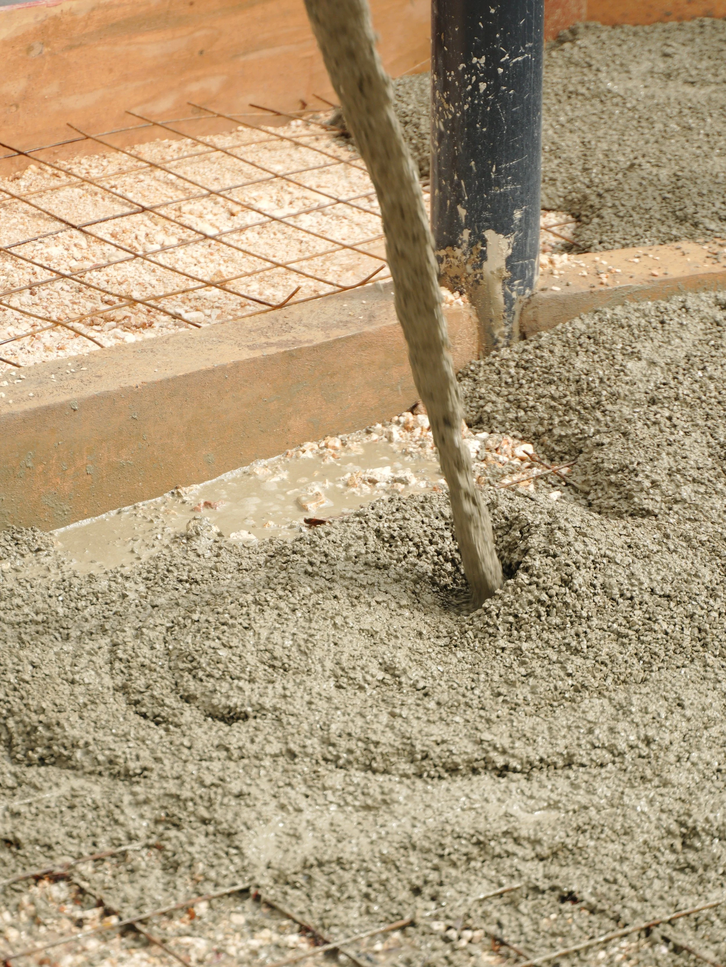 Pouring concrete into a prepared area with gravel and wire mesh on a construction site.