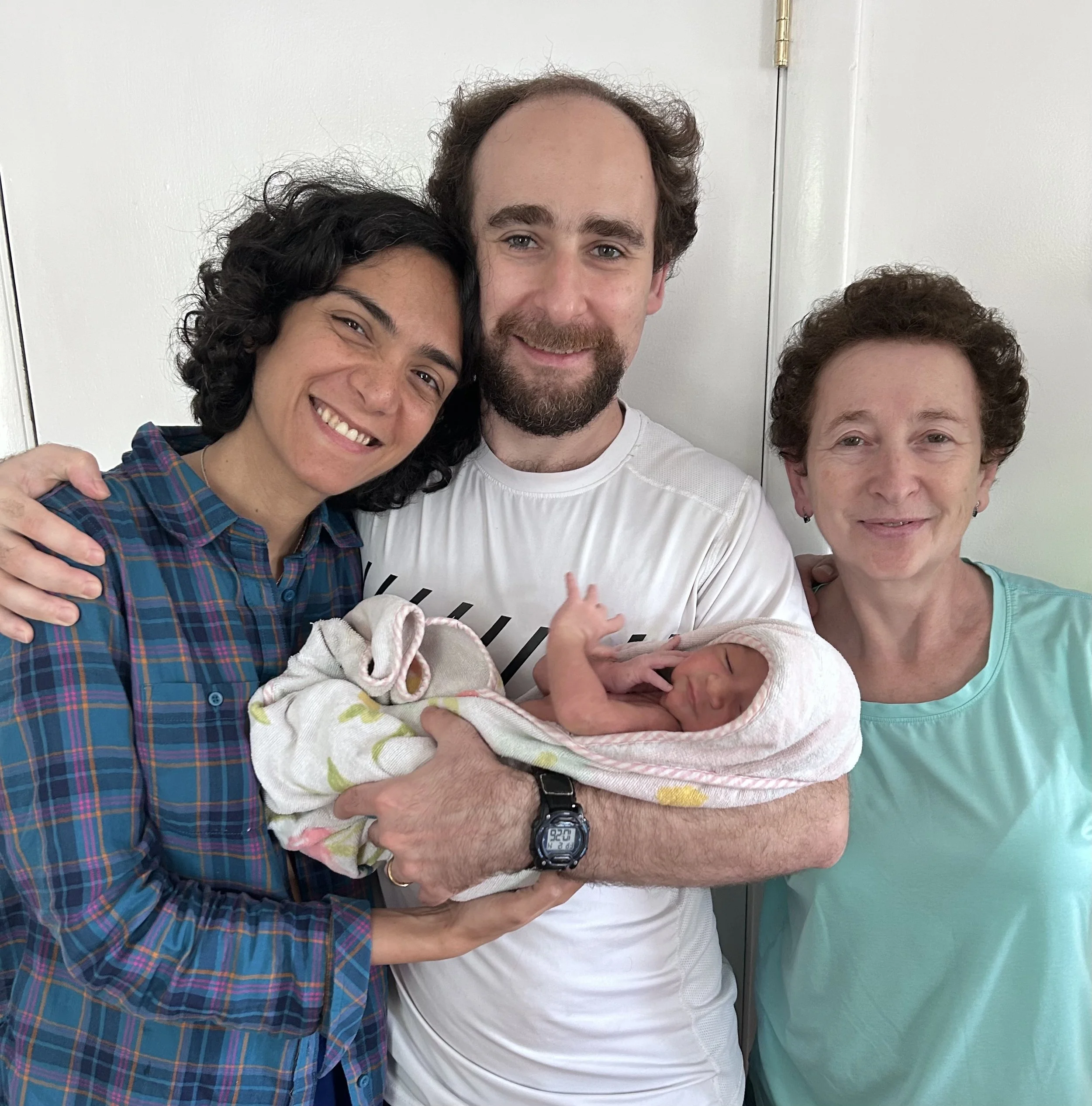 Family holding newborn baby in hospital room, smiling, celebrating birth.